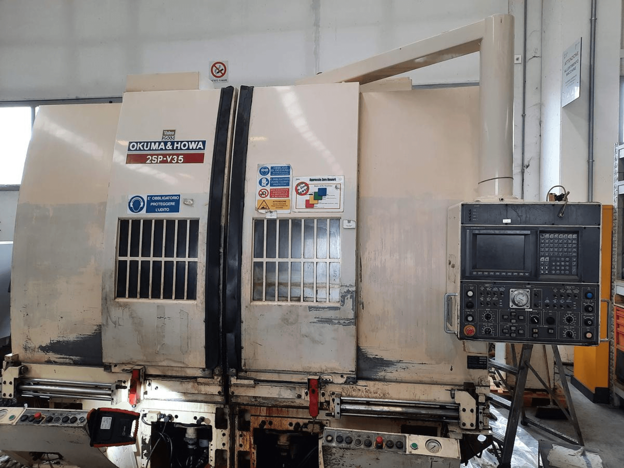 Maszyna CNC OKUMA & HOWA 2SP-V35 widziana od przodu, z panelem sterowania z różnymi przyciskami i etykietami bezpieczeństwa.