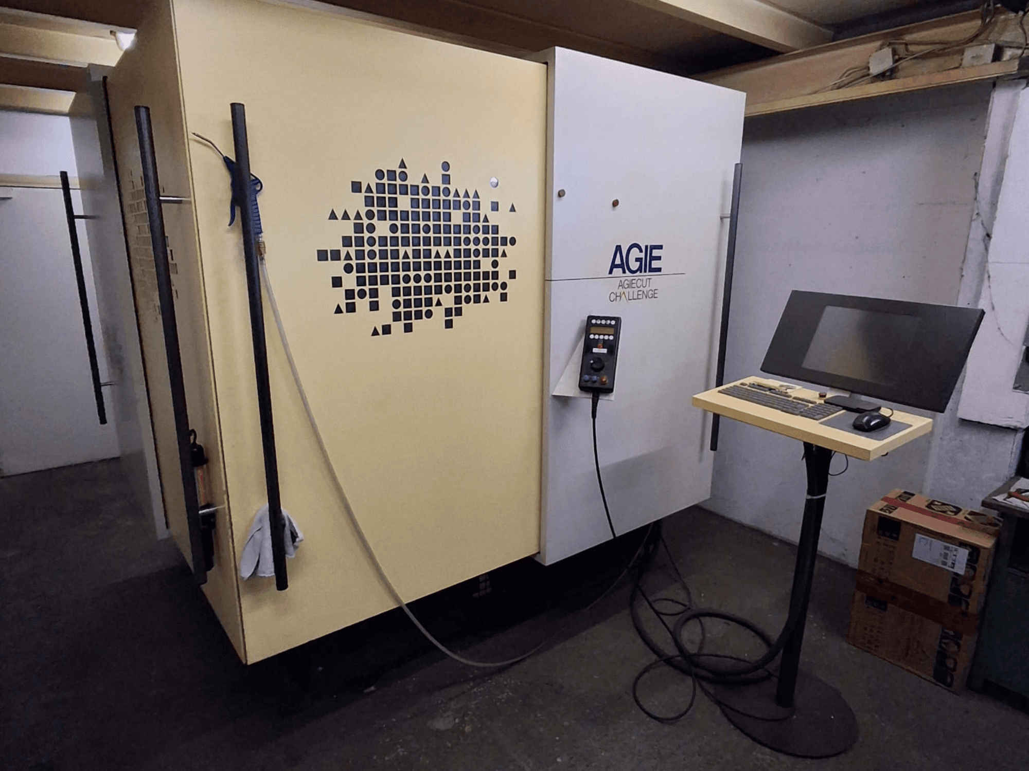 Maszyna do elektroerozji drutowej AGIE Agiecut Challenge 2 w warsztacie, z panelem sterowania i monitorem na stojaku – widok z przodu.