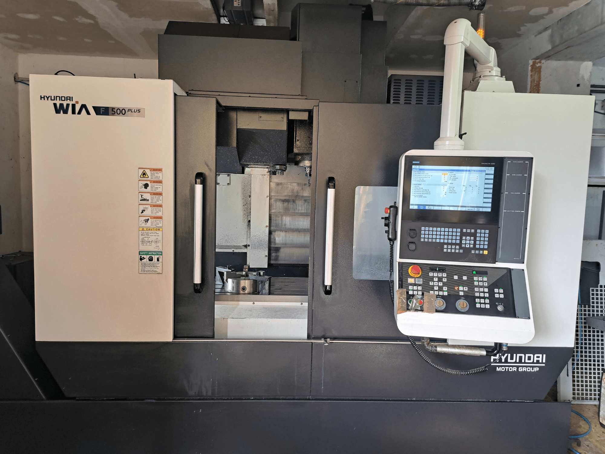 Maszyna CNC Hyundai WIA F500 Plus w widoku z przodu, z cyfrowym panelem sterowania i etykietami bezpieczeństwa.