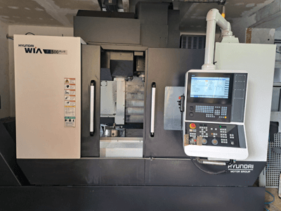 Maszyna CNC Hyundai WIA F500 Plus w widoku z przodu, z cyfrowym panelem sterowania i etykietami bezpieczeństwa.