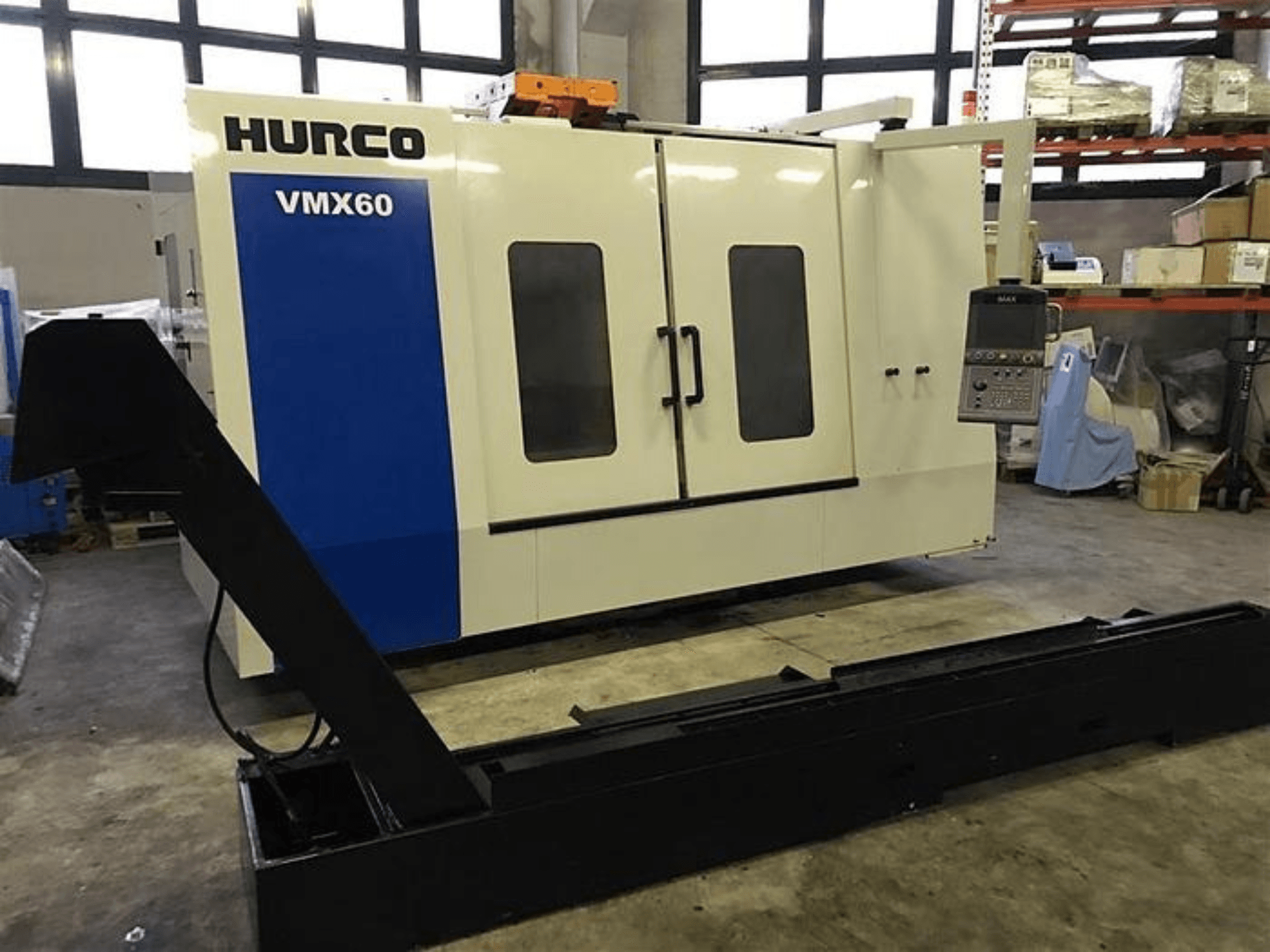 Maszyna CNC HURCO VMX60 w warsztacie, widok z przodu, z panelem sterowania i przymocowaną czarną szyną nośną.