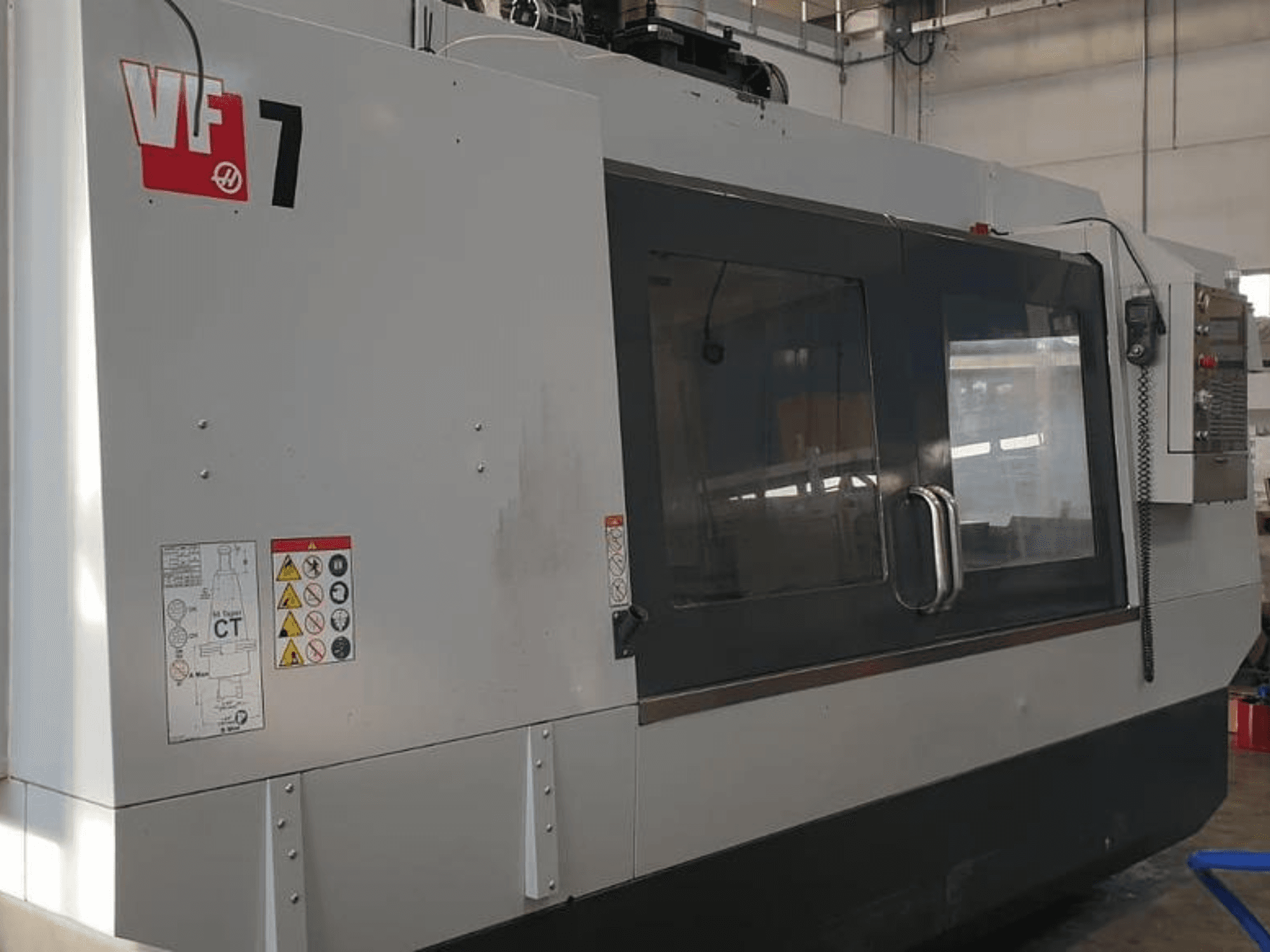 Maszyna CNC Haas VF-7 w widoku z boku, z metalowym szarym wykończeniem, panelem sterowania i etykietami bezpieczeństwa.