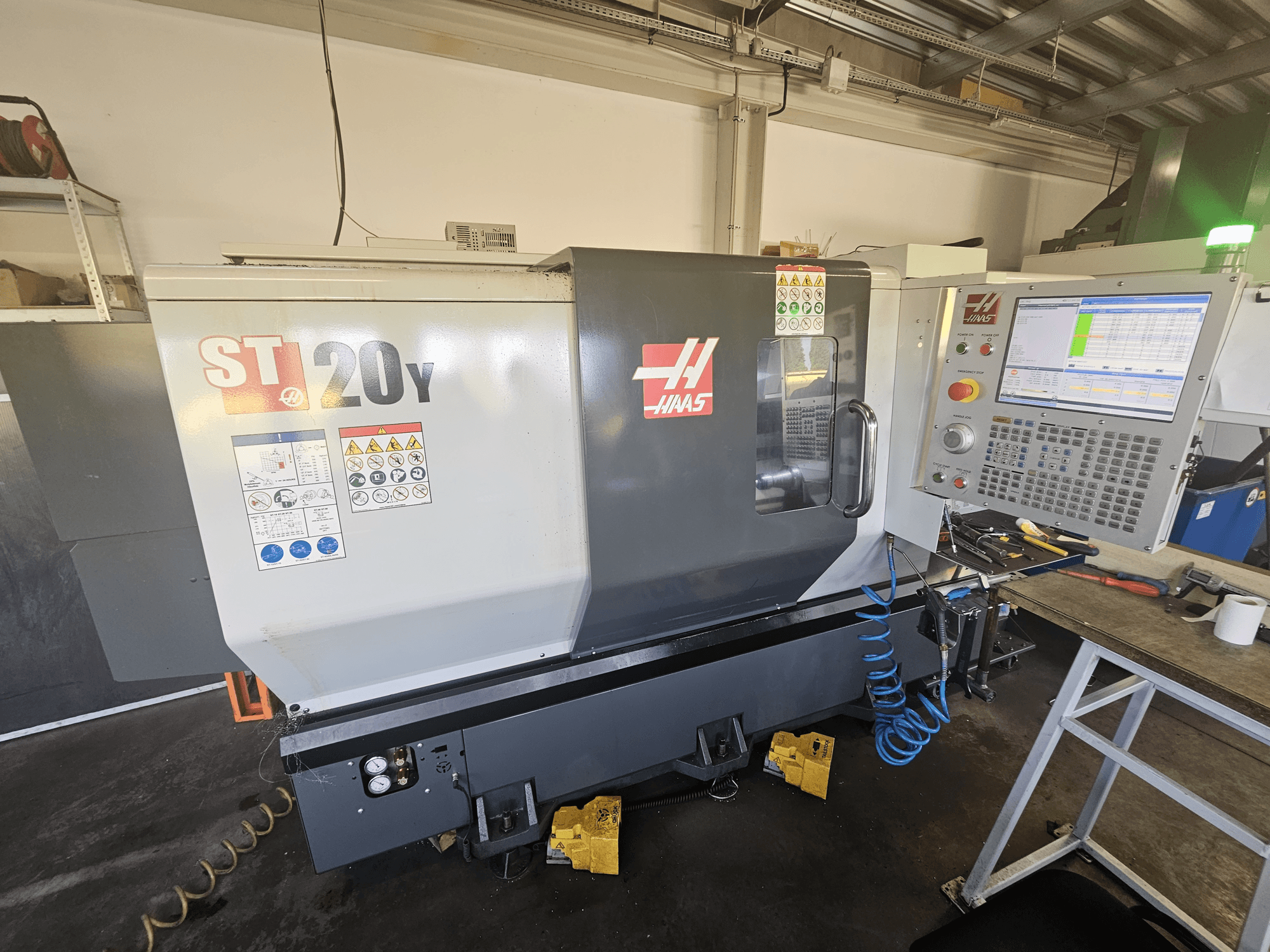 Tokarka CNC Haas ST-20Y w widoku z przodu z panelem sterowania; zawiera etykiety bezpieczeństwa i szczegóły węża powietrza z boku.