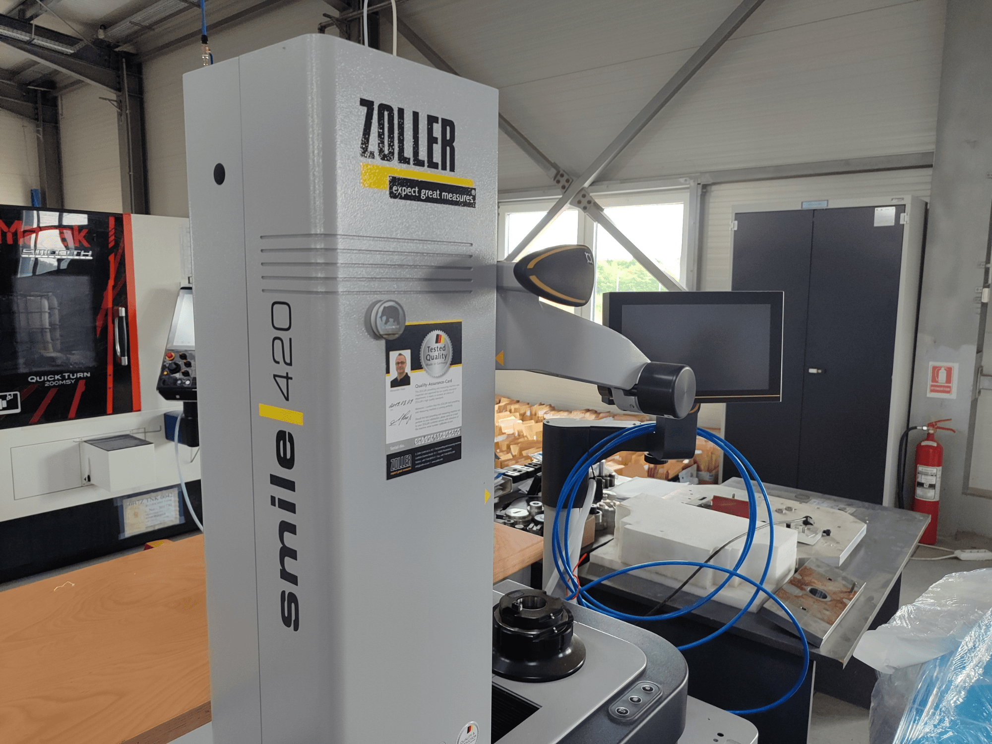 Urządzenie pomiarowe ZOLLER smile 420 z monitorem, widok z boku w warsztacie, z niebieskimi wężami i maszynami w tle.