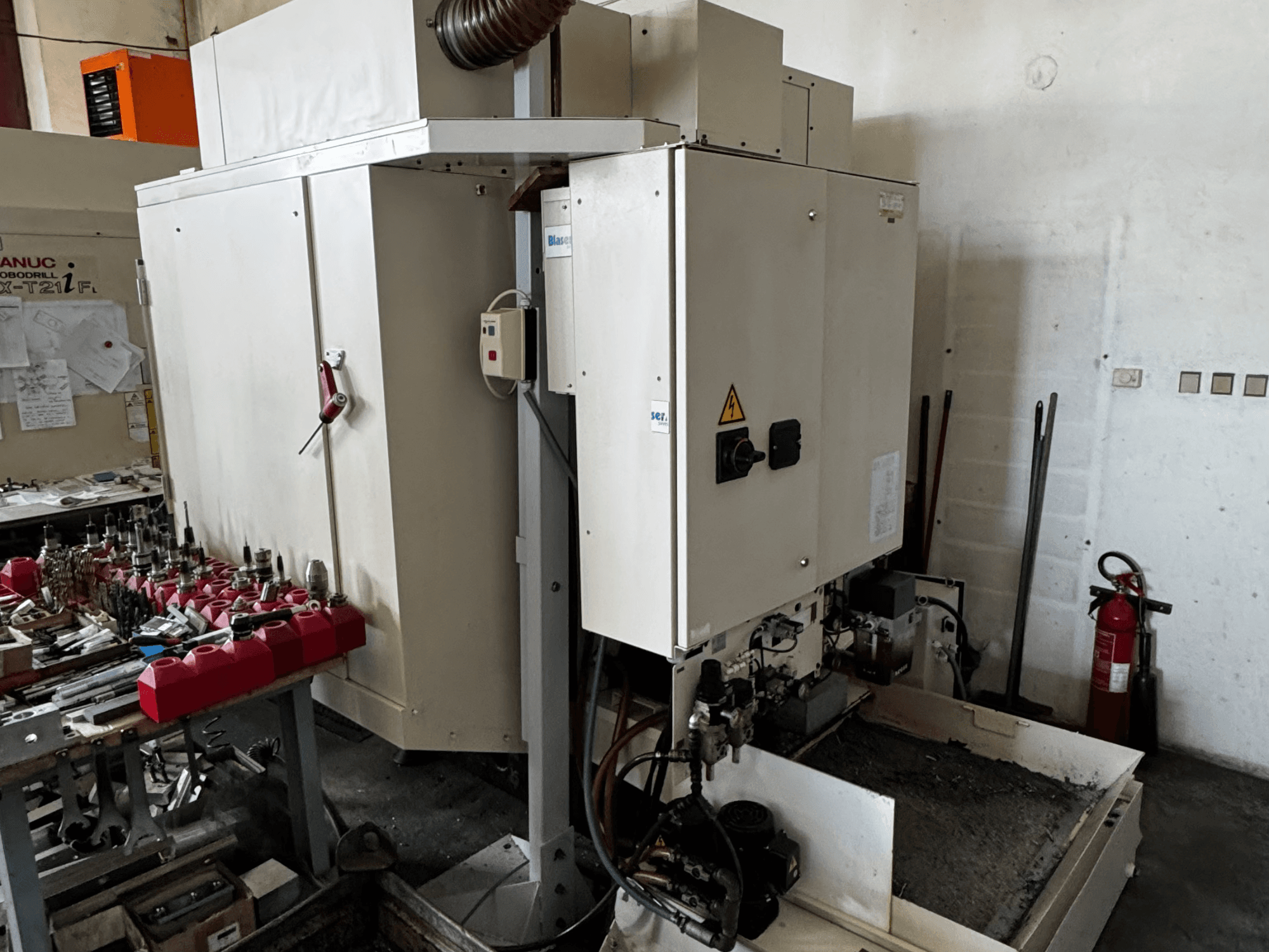 Pionowe centrum obróbcze FANUC Robodrill alpha-T21iFL, widok z boku przedstawiający panel sterowania, narzędzia i obszar roboczy.