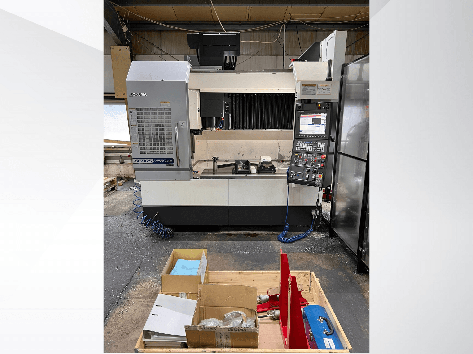 Pionowe centrum obróbcze Okuma GENOS M460V-5, widok z przodu, widoczny panel sterowania i narzędzia na stole roboczym.