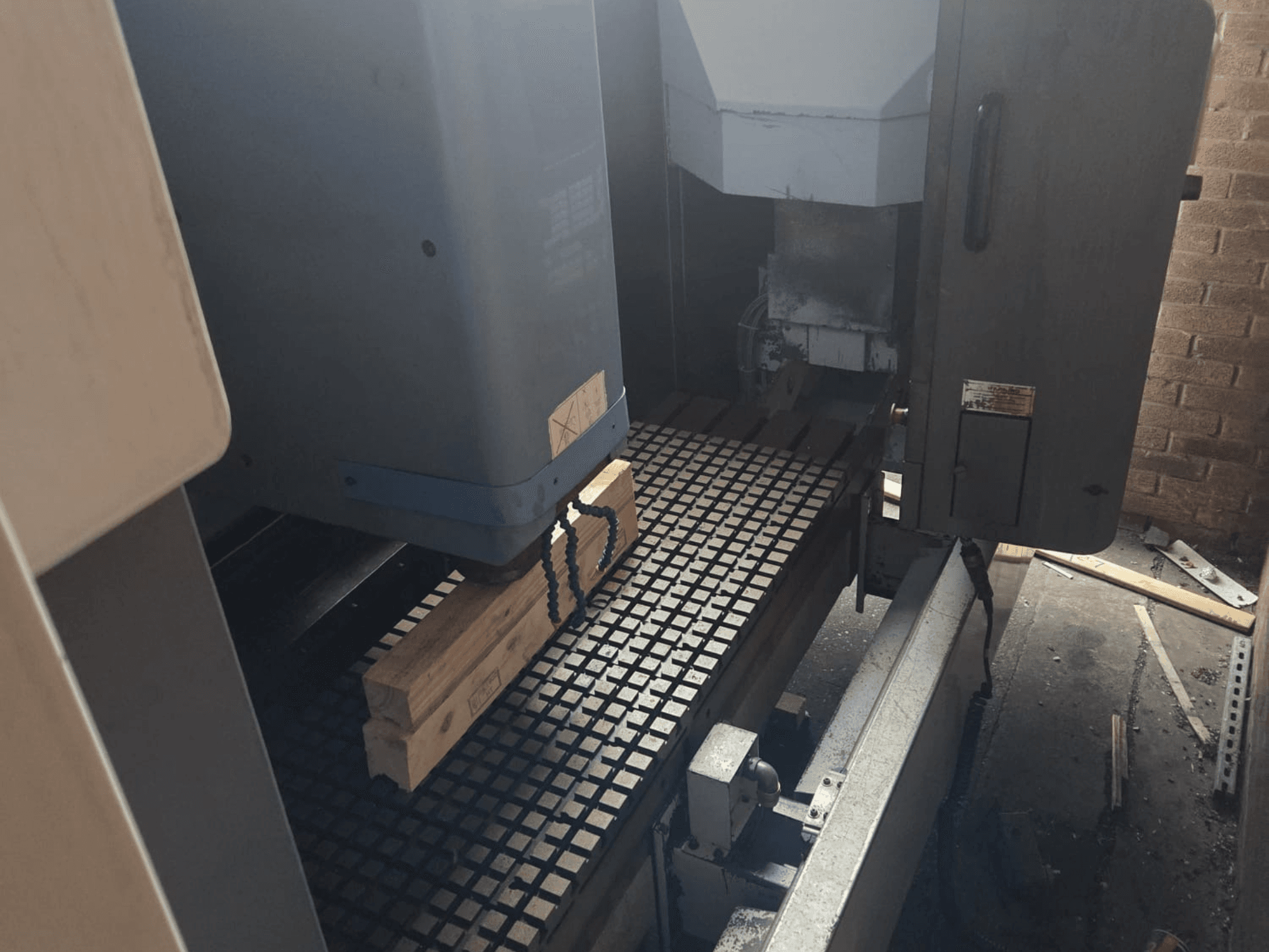 Widok z przodu maszyny CNC z drewnianymi deskami na stole siatkowym, z narzędziami i elementami sterującymi z boku.