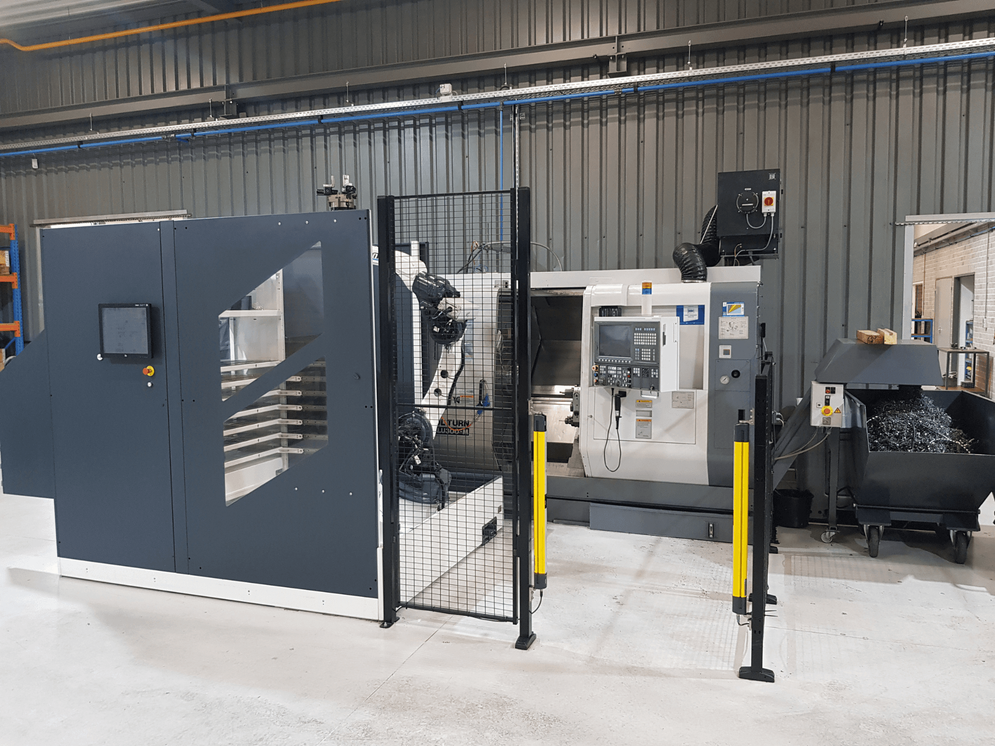 Zautomatyzowana tokarka ALTURN i maszyna CNC pokazane w ustawieniu fabrycznym; widok z przodu z widocznym panelem sterowania i ogrodzeniem ochronnym.