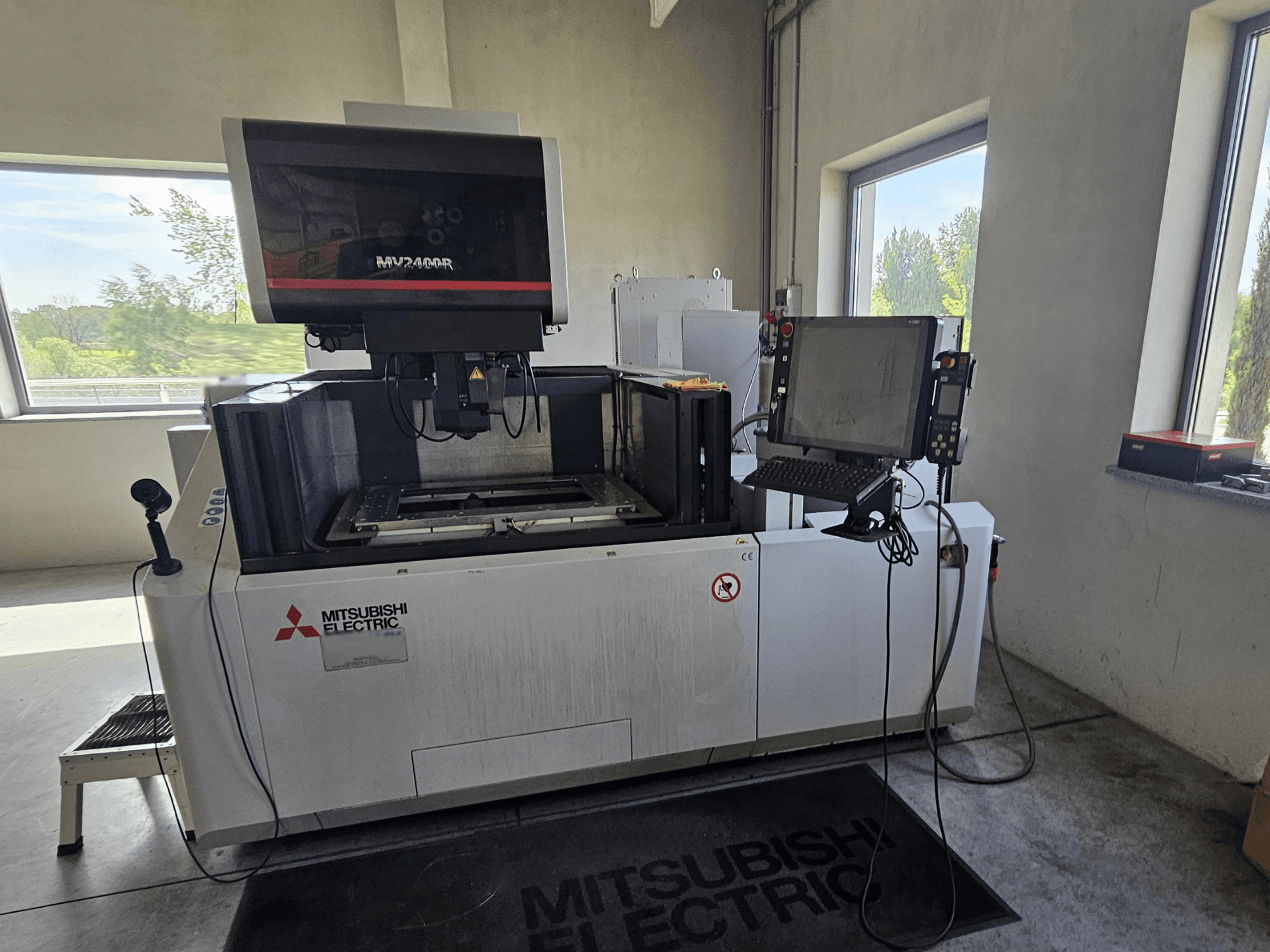Elektrodrążarka drutowa Mitsubishi MV2400R w warsztacie, z panelem sterowania z ekranem dotykowym i obszarem roboczym.