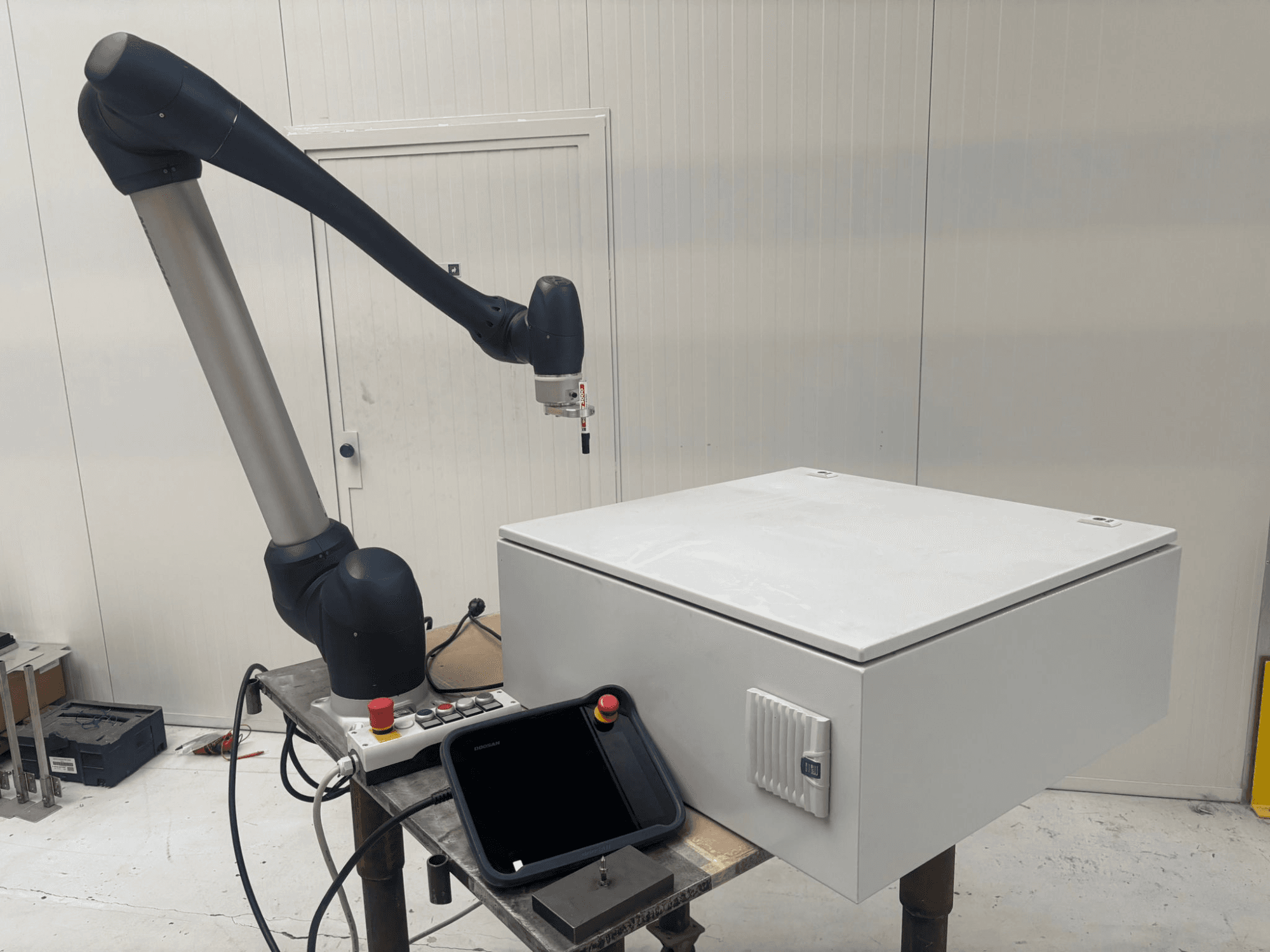 Robot współpracujący DOOSAN M0617 w widoku z boku, z ramieniem robota wyciągniętym nad interfejsem sterowania i białym pudełkiem na stole.