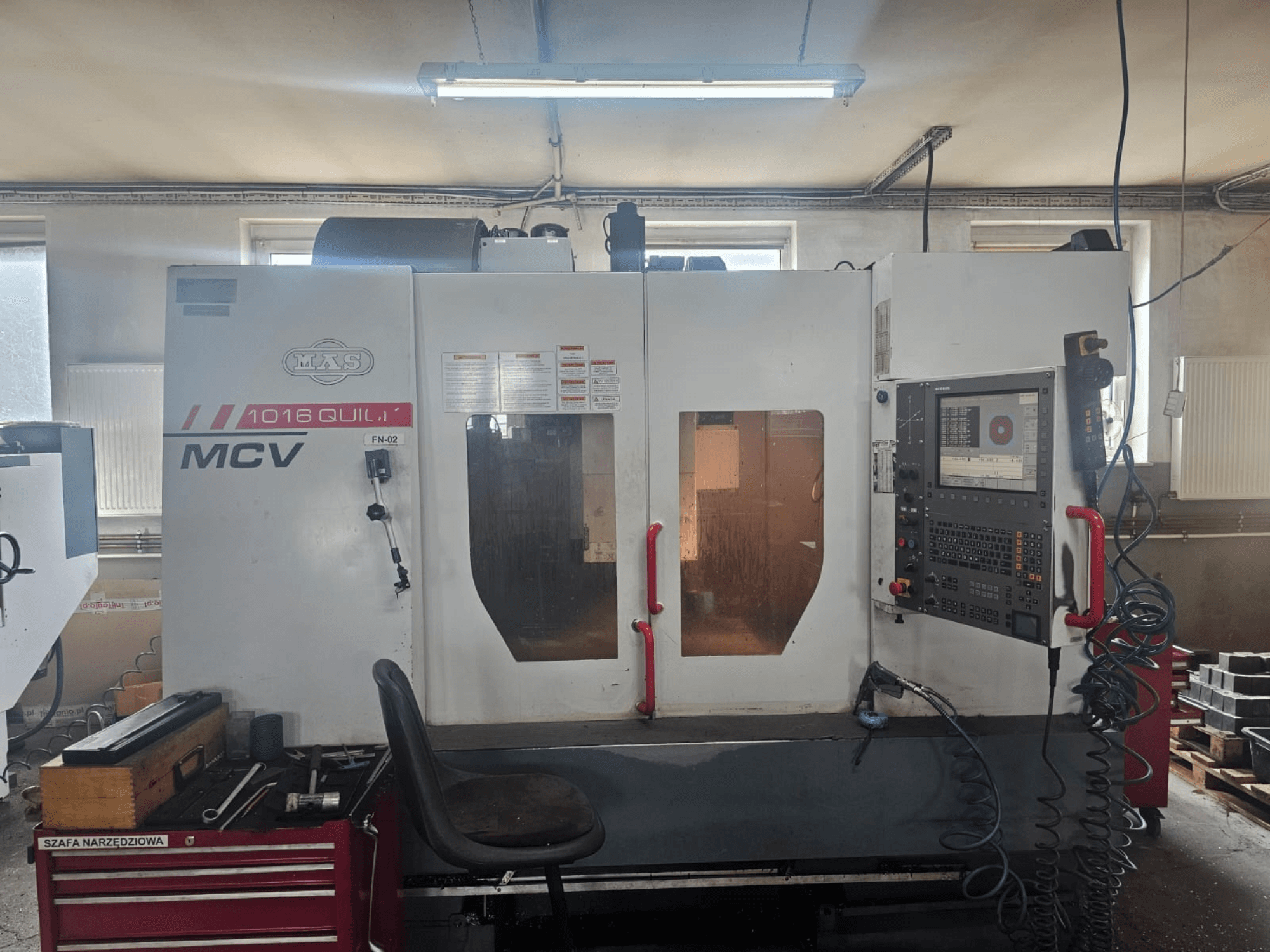 Maszyna CNC MVS MCV 1016 QUILL, widok z przodu, z panelem sterowania, szufladą na narzędzia i obszarem roboczym z narzędziami.