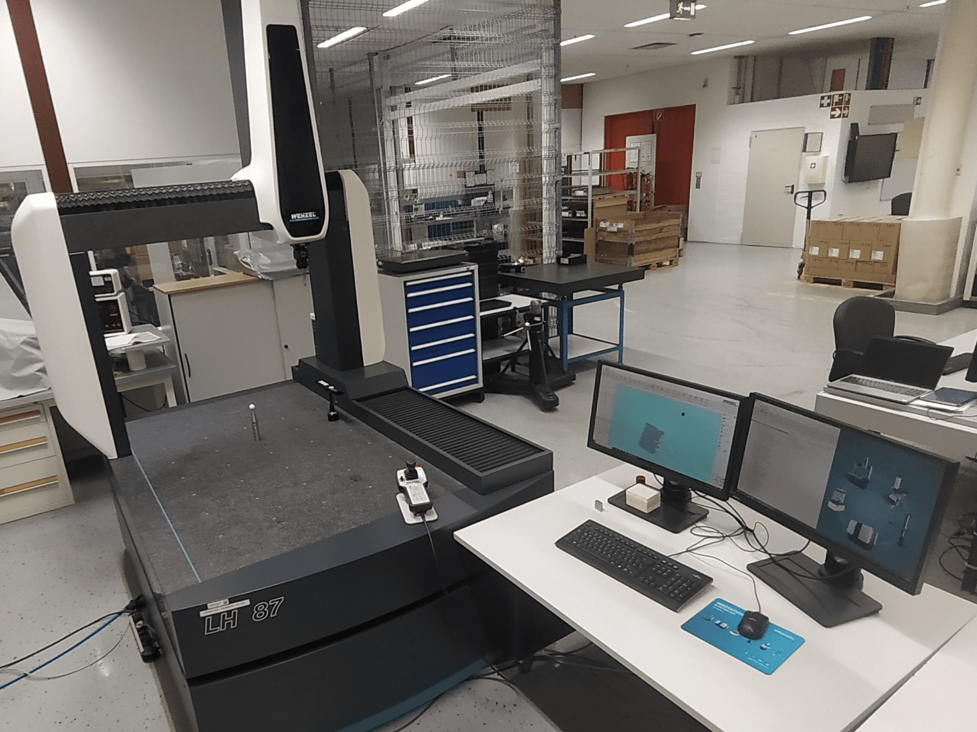 Współrzędnościowa maszyna pomiarowa Wenzel LH 87 widoczna w warunkach laboratoryjnych, z dwoma monitorami i sondą pomiarową na stole.