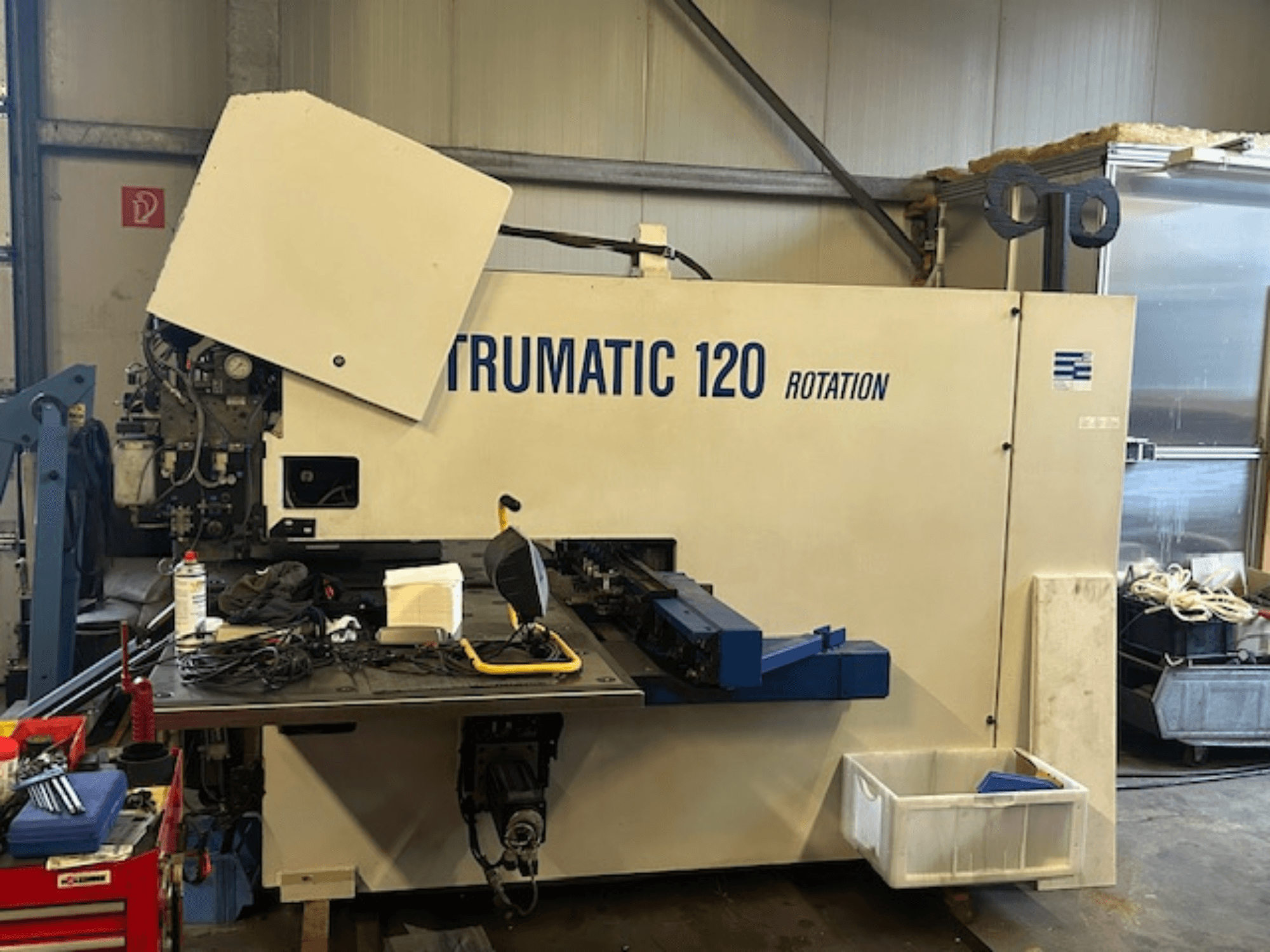 Wykrawarka CNC TRUMPF Trumatic 120R w warsztacie, widok z przodu przedstawiający panel sterowania i narzędzia na stole.