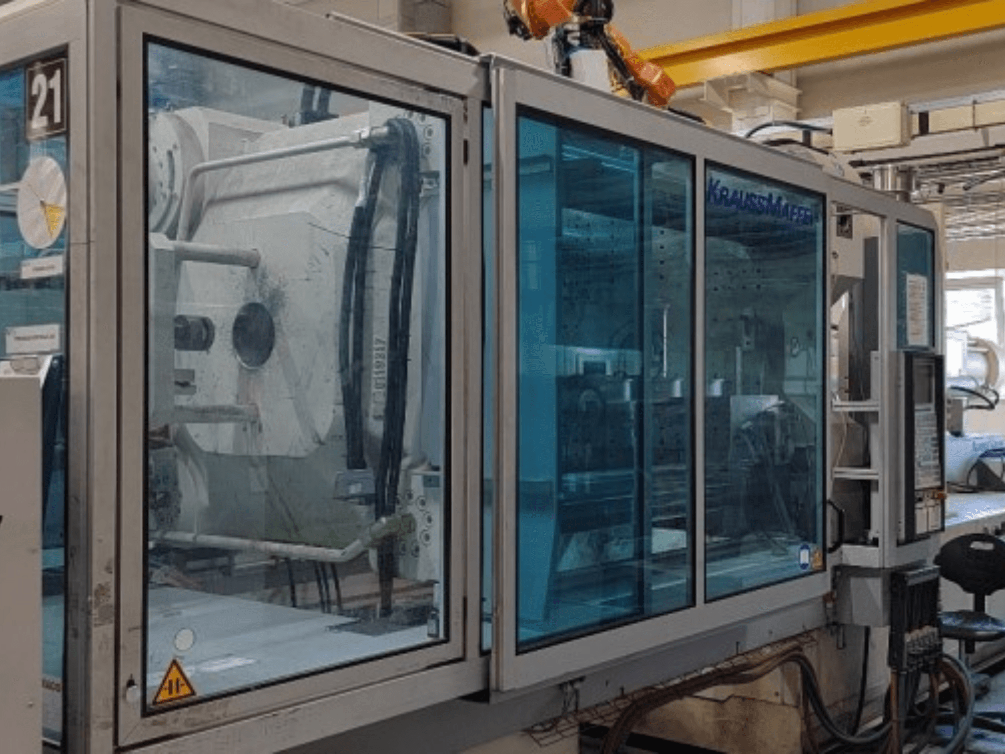 Hydrauliczna wtryskarka Krauss Maffei KM 575-2700 C2, widok z boku, wyposażona w przezroczyste panele ochronne i panel sterowania.
