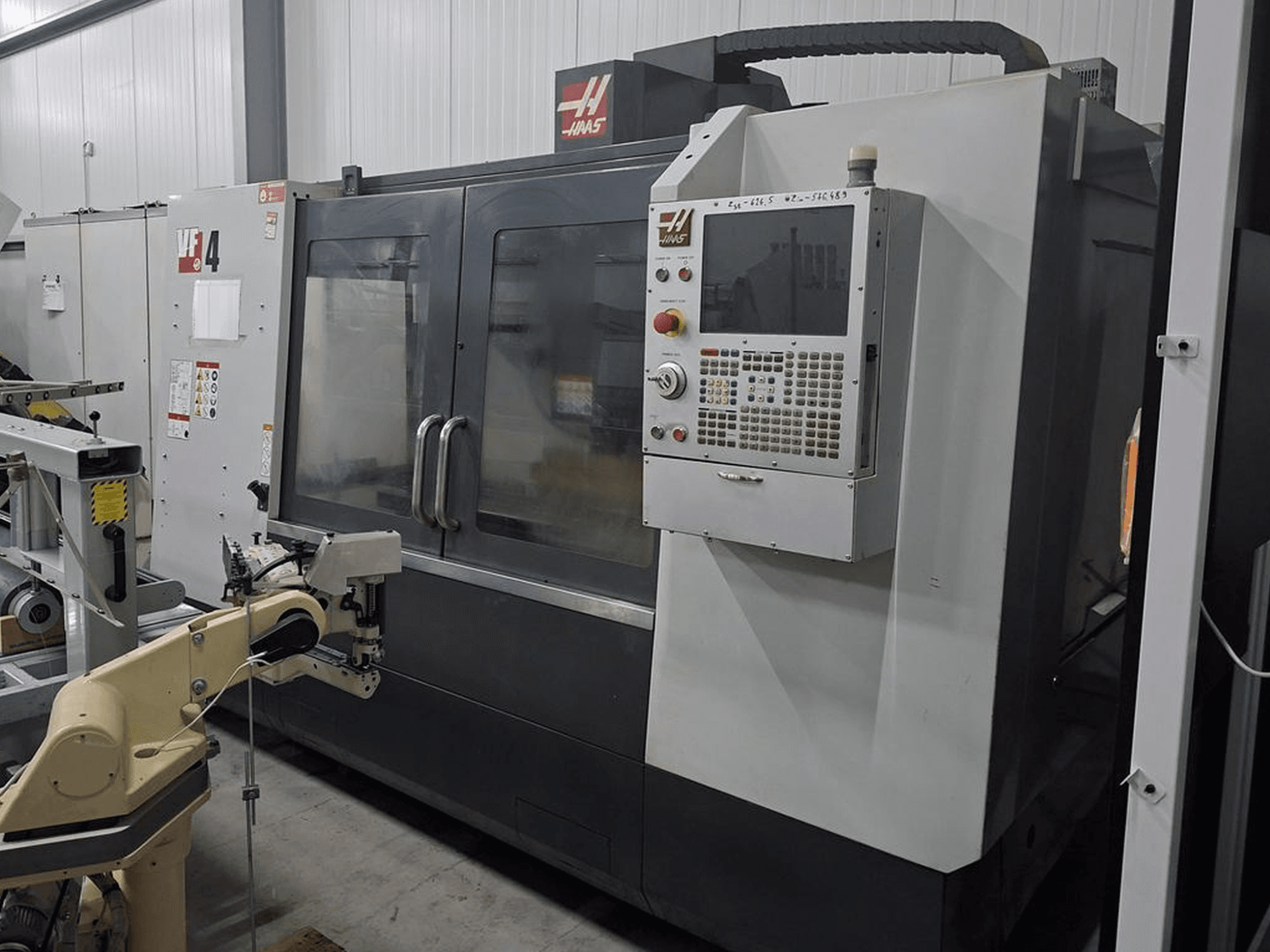 Frezarka CNC Haas VF-4 w widoku z przodu, wyposażona w numeryczny panel sterowania i ramię robota do automatyzacji.