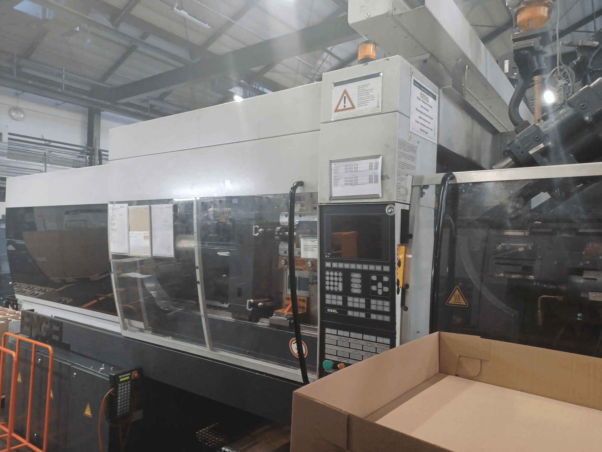 Wtryskarka Engel, widok z przodu, z panelem sterowania, etykietami bezpieczeństwa i pustym pudełkiem umieszczonym w pobliżu.