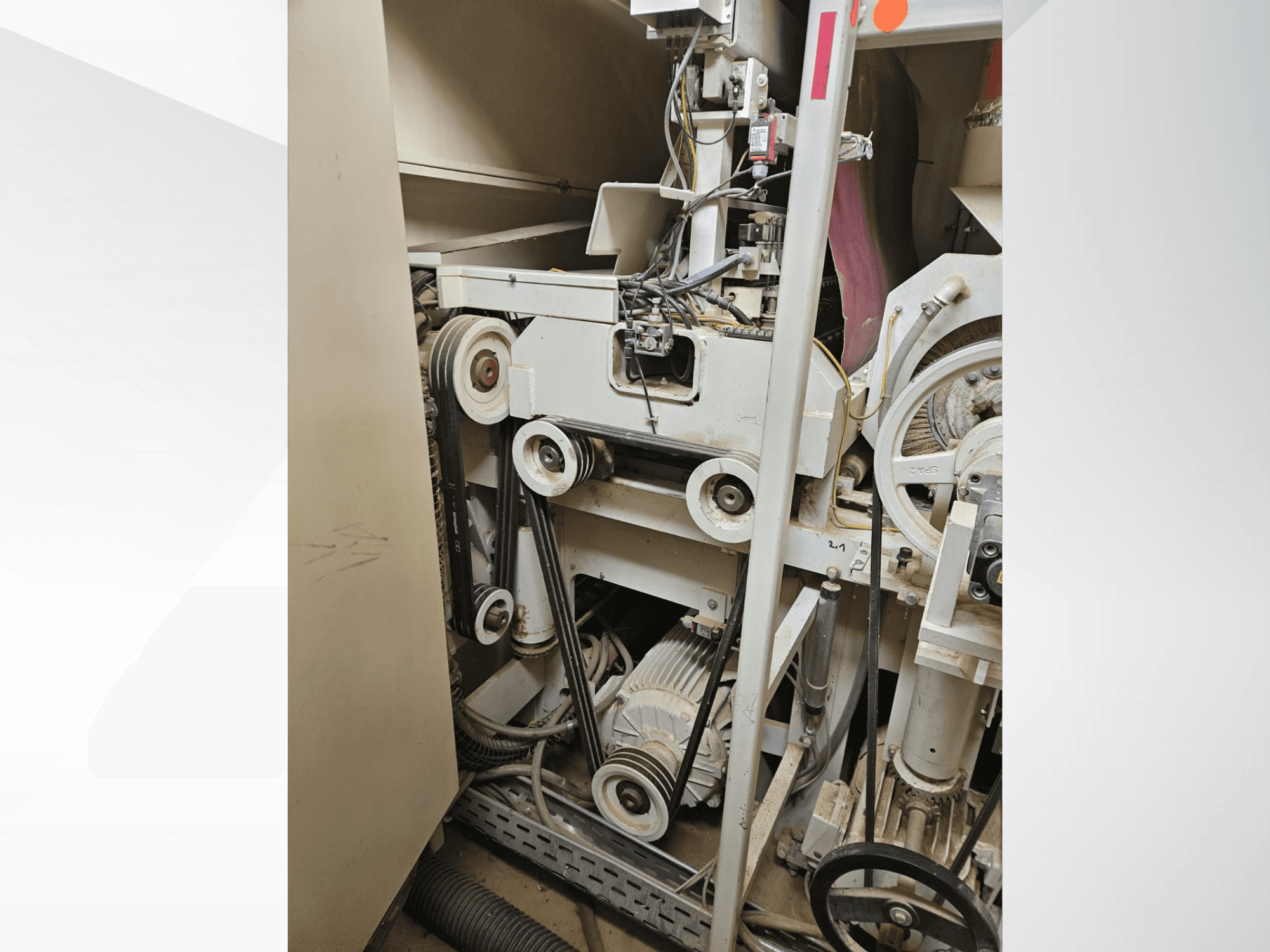 Wnętrze maszyny przemysłowej z pasami i kołami pasowymi, z silnikiem i okablowaniem, widziane z boku.