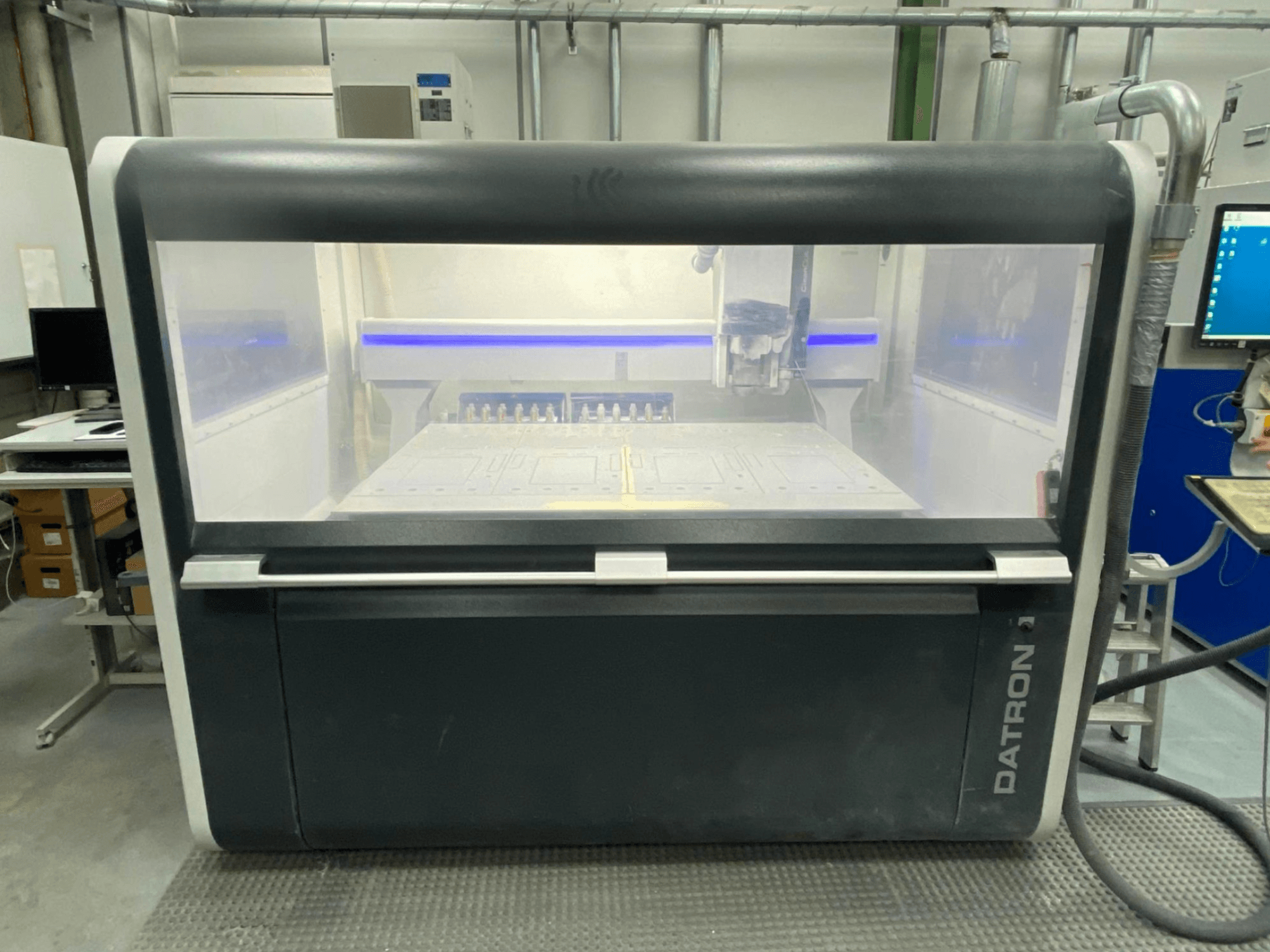 Widok z przodu pionowego centrum obróbczego Datron MLCube B z przezroczystą obudową i panelem sterowania.