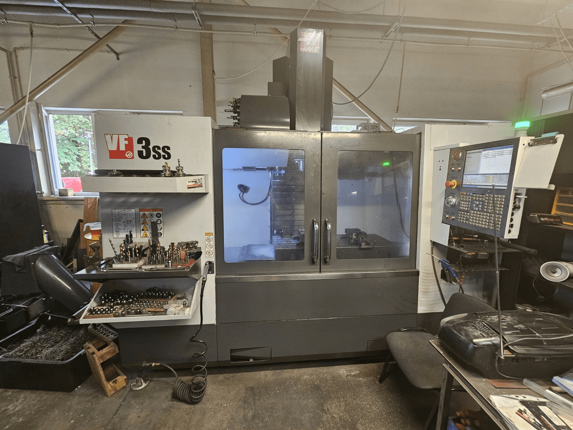 Pionowe centrum obróbcze Haas VF-3SS w warsztacie – widok z przodu przedstawiający panel sterowania i schowek na narzędzia.