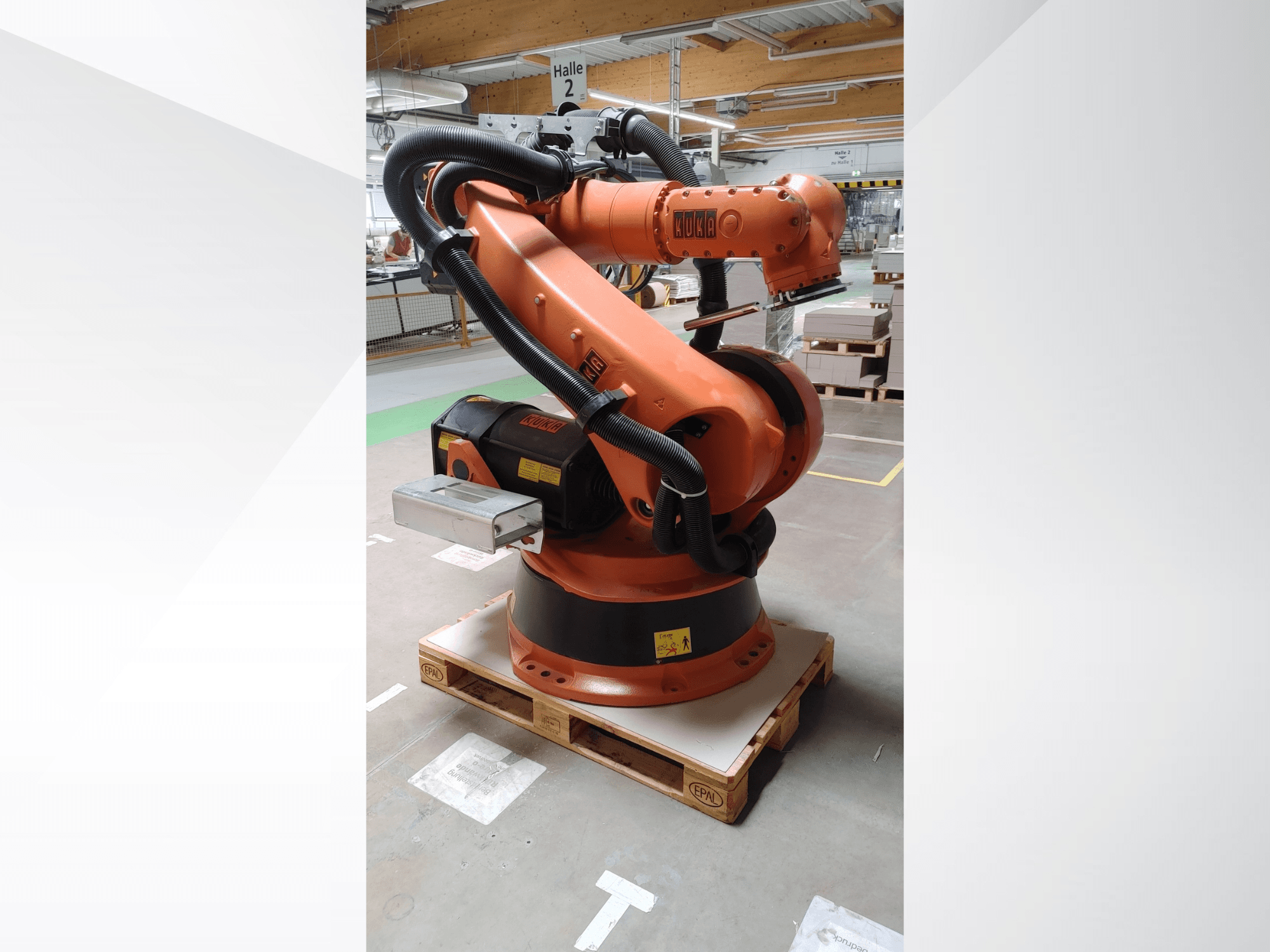 Ramię robota KUKA KR140-3 COMP w kolorze pomarańczowym, widok z przodu na drewnianej palecie, z zakrzywionym ramieniem i skrzynką kontrolną.
