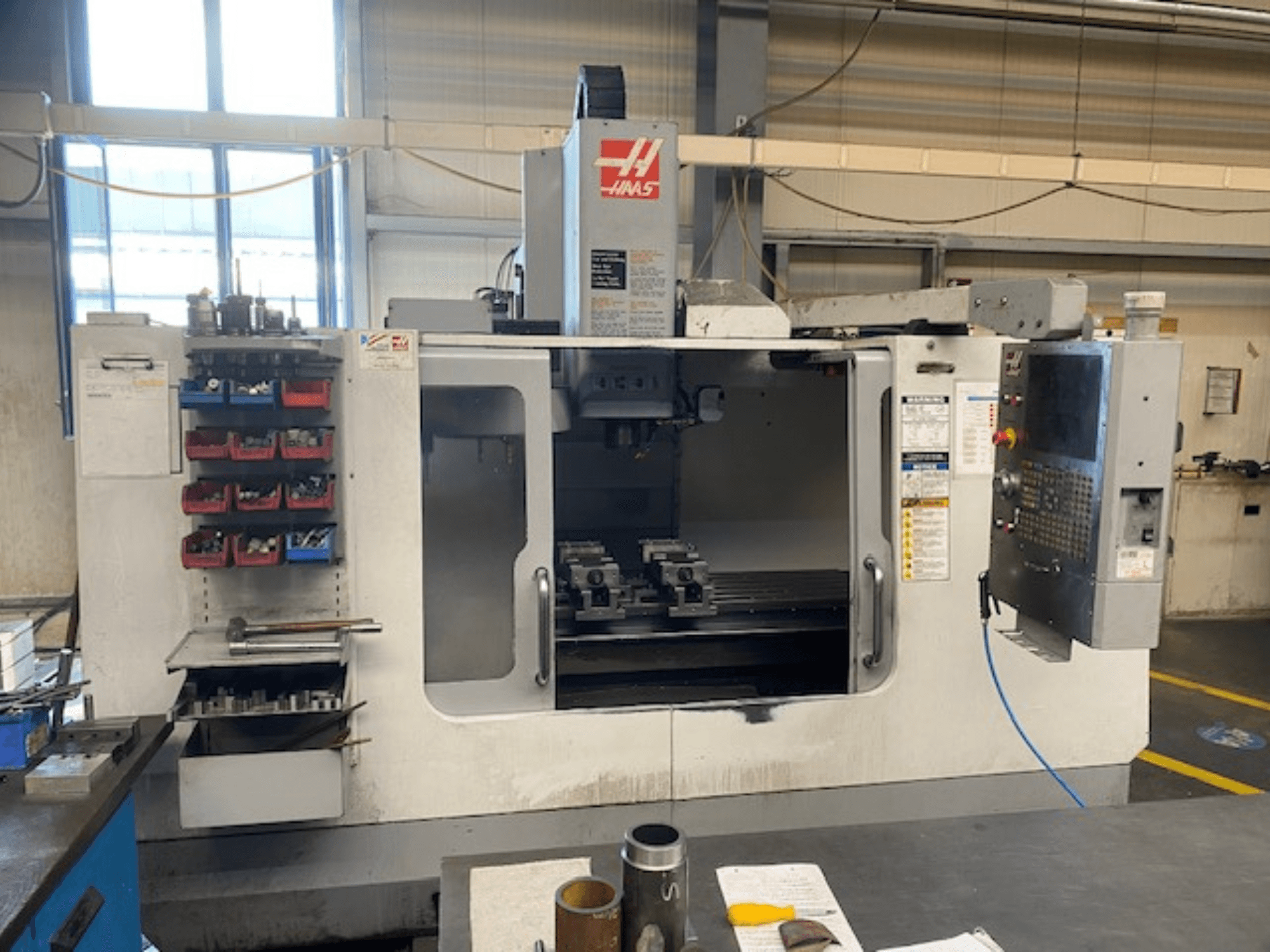 Widok z przodu frezarki CNC firmy Haas, model VF-2, z widocznym magazynem narzędzi, panelem sterowania i narzędziami w obszarze roboczym.