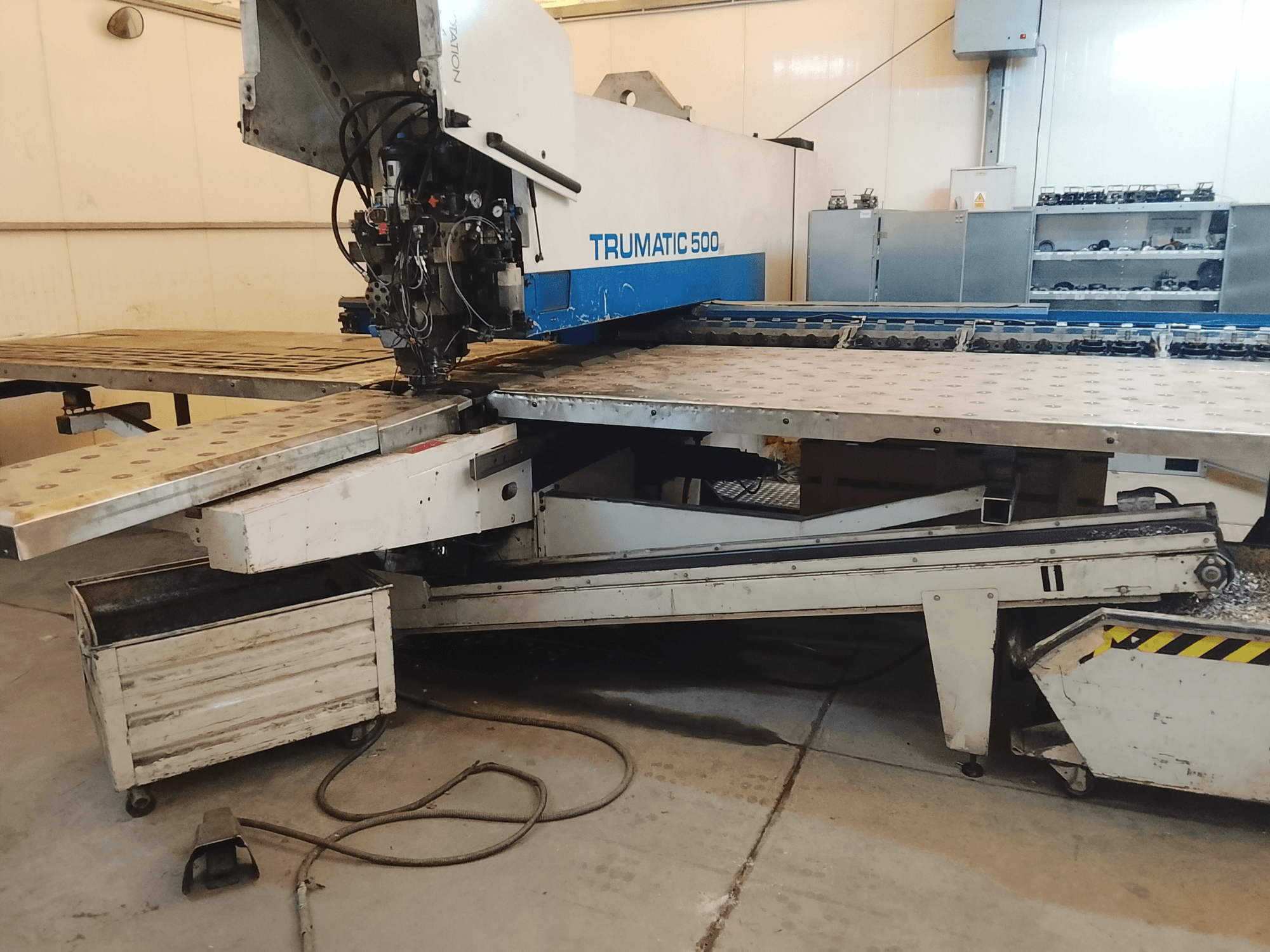 Maszyna CNC TRUMATIC 500 w warsztacie, widok z boku pokazujący głowicę tnącą i metalowy stół roboczy z nawierconymi otworami.