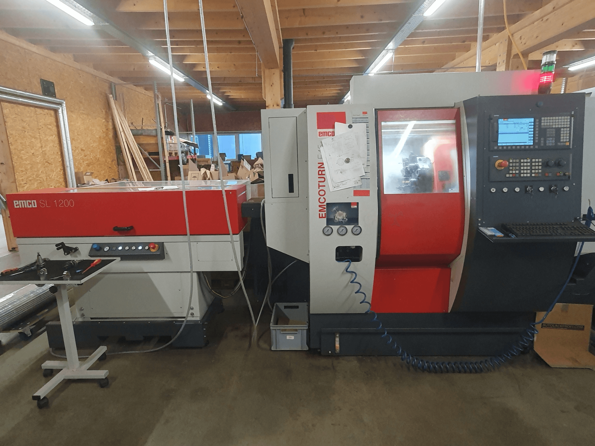 Tokarka CNC EMCO SL 1200 i EMCOturn; widok z przodu przedstawiający elementy sterujące, wyświetlacze i wskaźniki operacyjne w warunkach warsztatowych.