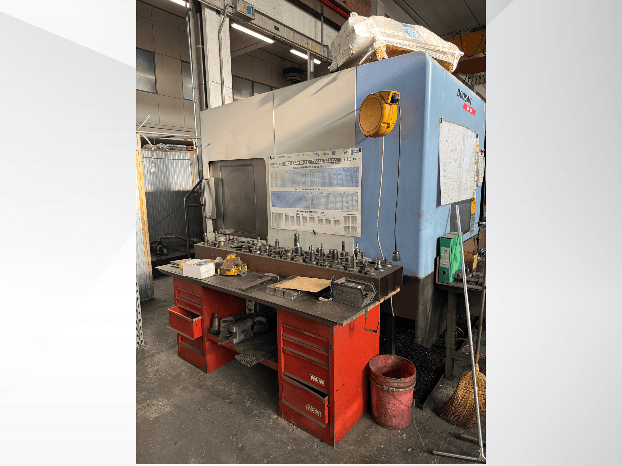 Centrum obróbcze Doosan z czerwonym stołem roboczym i schowkiem na narzędzia i sprzęt, widziane od przodu.