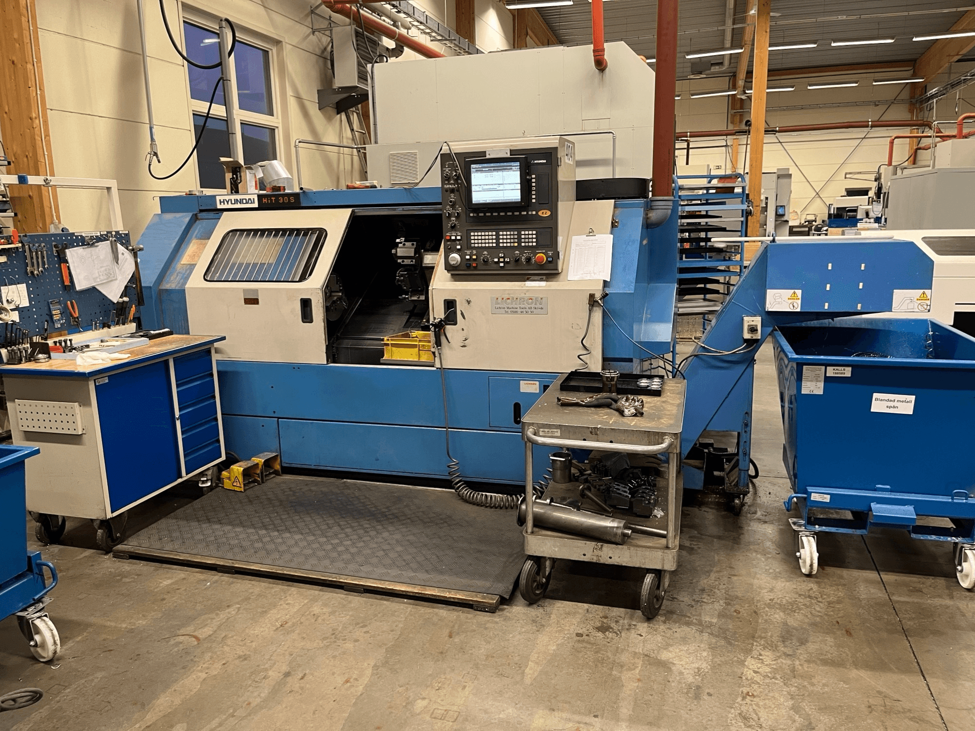 Tokarka pozioma Hyundai HIT 30S, widok z przodu, z panelem sterowania i narzędziami na pobliskim wózku w warunkach warsztatowych.