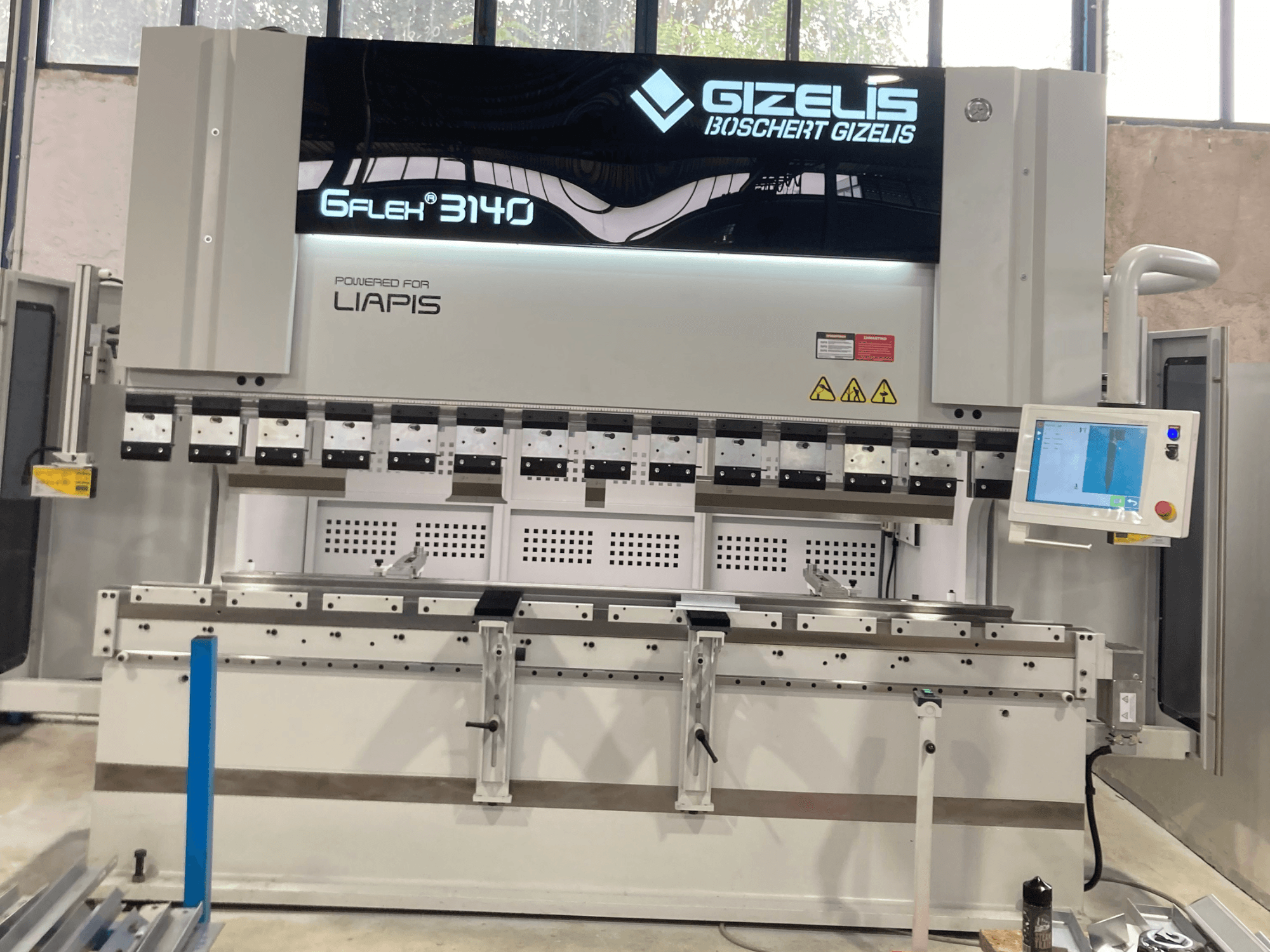 Prasa hydrauliczna GIZELIS G-FLEX 3140 w widoku z przodu z ekranem sterowania, wyposażona w wiele narzędzi do gięcia i etykiety bezpieczeństwa.