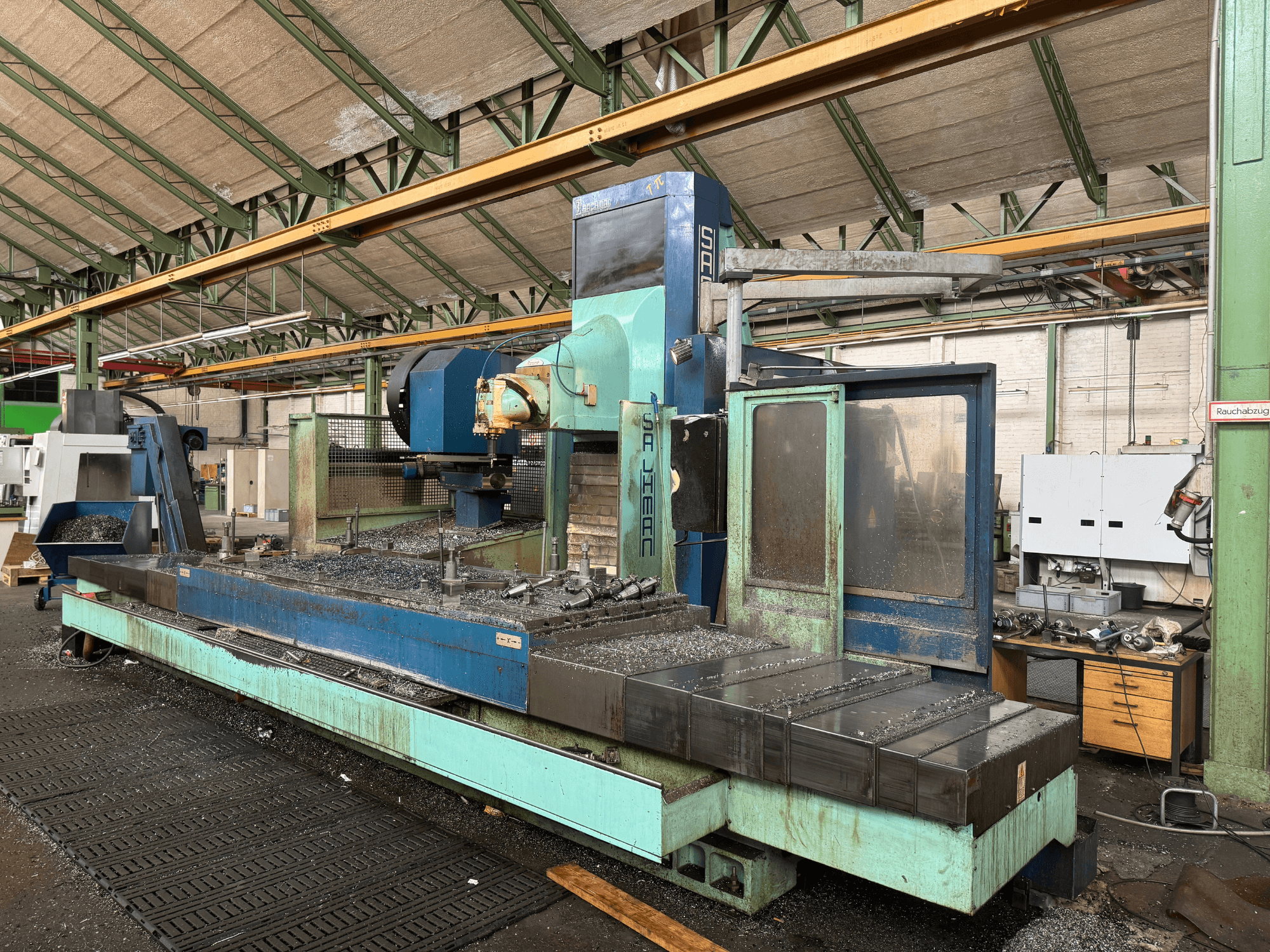 Frezarka Salvador w ustawieniu fabrycznym, widok z przodu, w niebiesko-zielonej kolorystyce, pokazująca metalowe wióry na łożu.