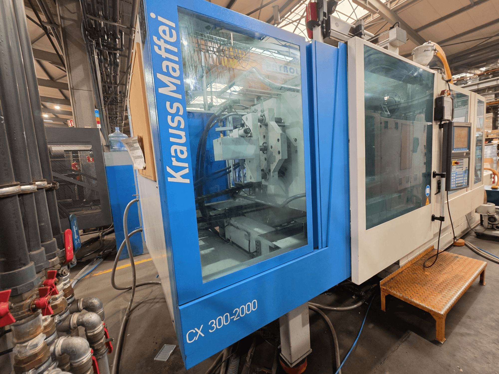 Hydrauliczna wtryskarka Krauss Maffei CX 300-2000, widok z przodu, pokazujący panel sterowania i przewody hydrauliczne.