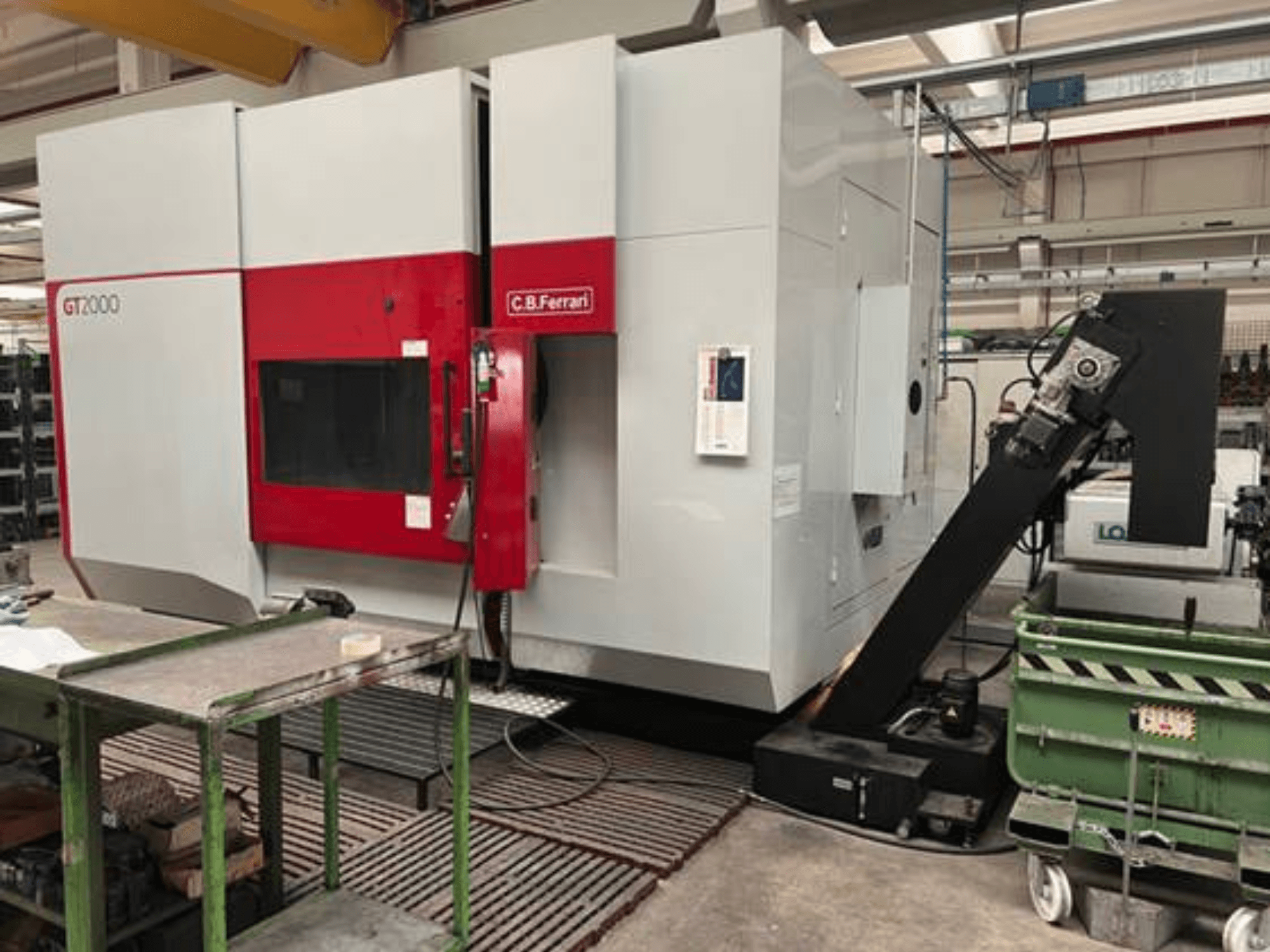 Frezarka C.B. Ferrari GT2000 w widoku z przodu, wyposażona w ramię robotyczne i przemysłową przestrzeń roboczą z zielonym wózkiem.