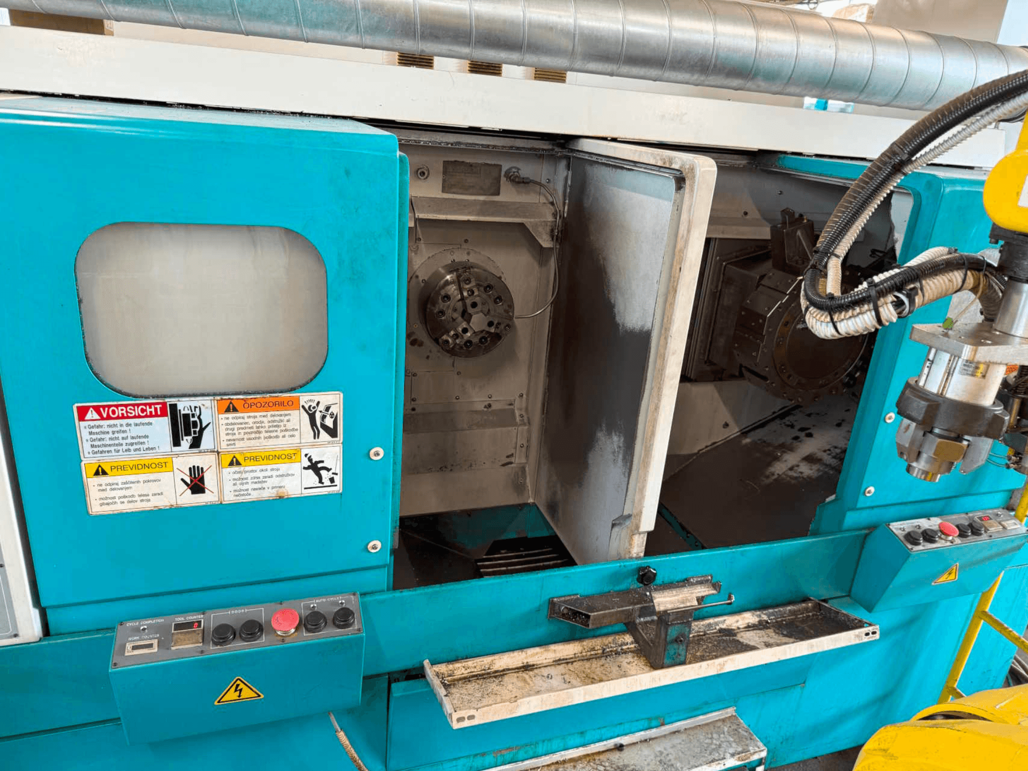 Tokarka pozioma DOOSAN H310T, widok z przodu przedstawiający panel sterowania i obszar wrzeciona z ostrzeżeniami dotyczącymi bezpieczeństwa.