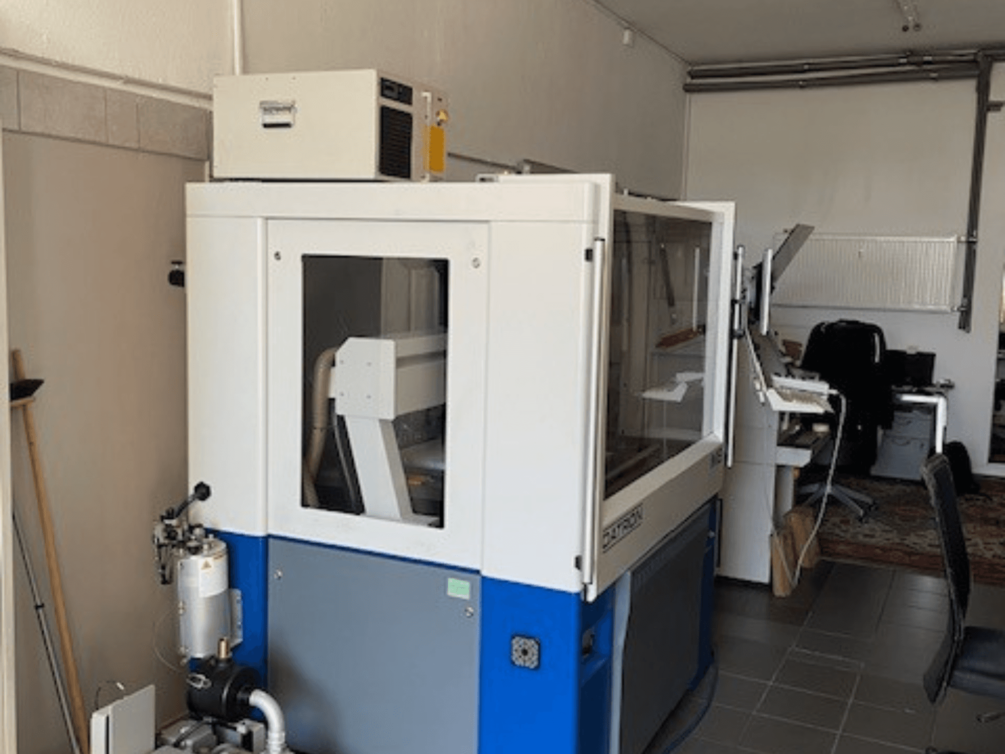 Niebiesko-biała maszyna przemysłowa z przezroczystymi panelami, widok z przodu, zawiera dostęp do sterowania i widoczną jednostkę wentylacyjną.
