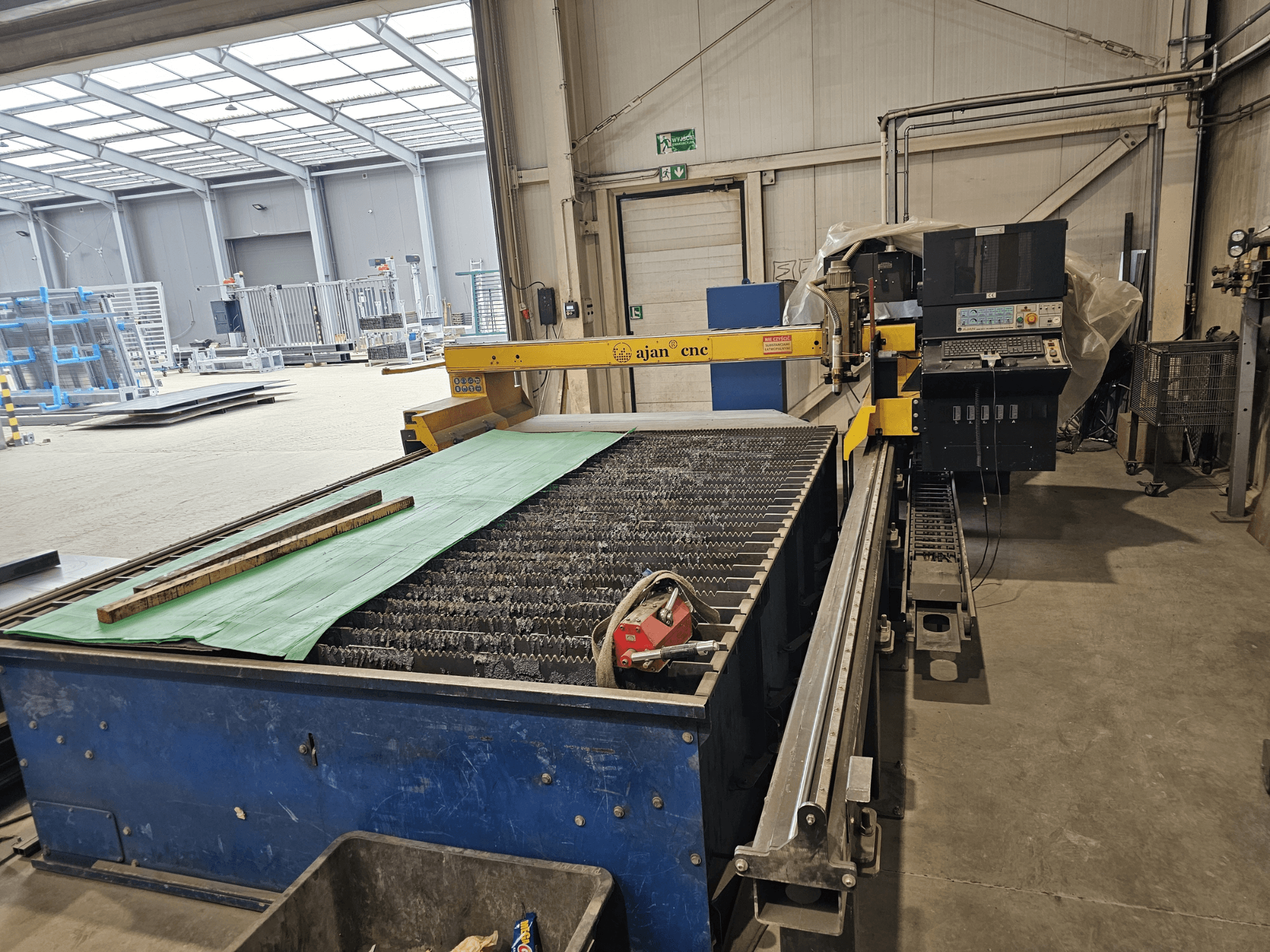 Automatyczna przecinarka plazmowa AJAN PP16011 w widoku z boku, ze stołem do cięcia i panelem sterowania, ustawiona w środowisku warsztatowym.