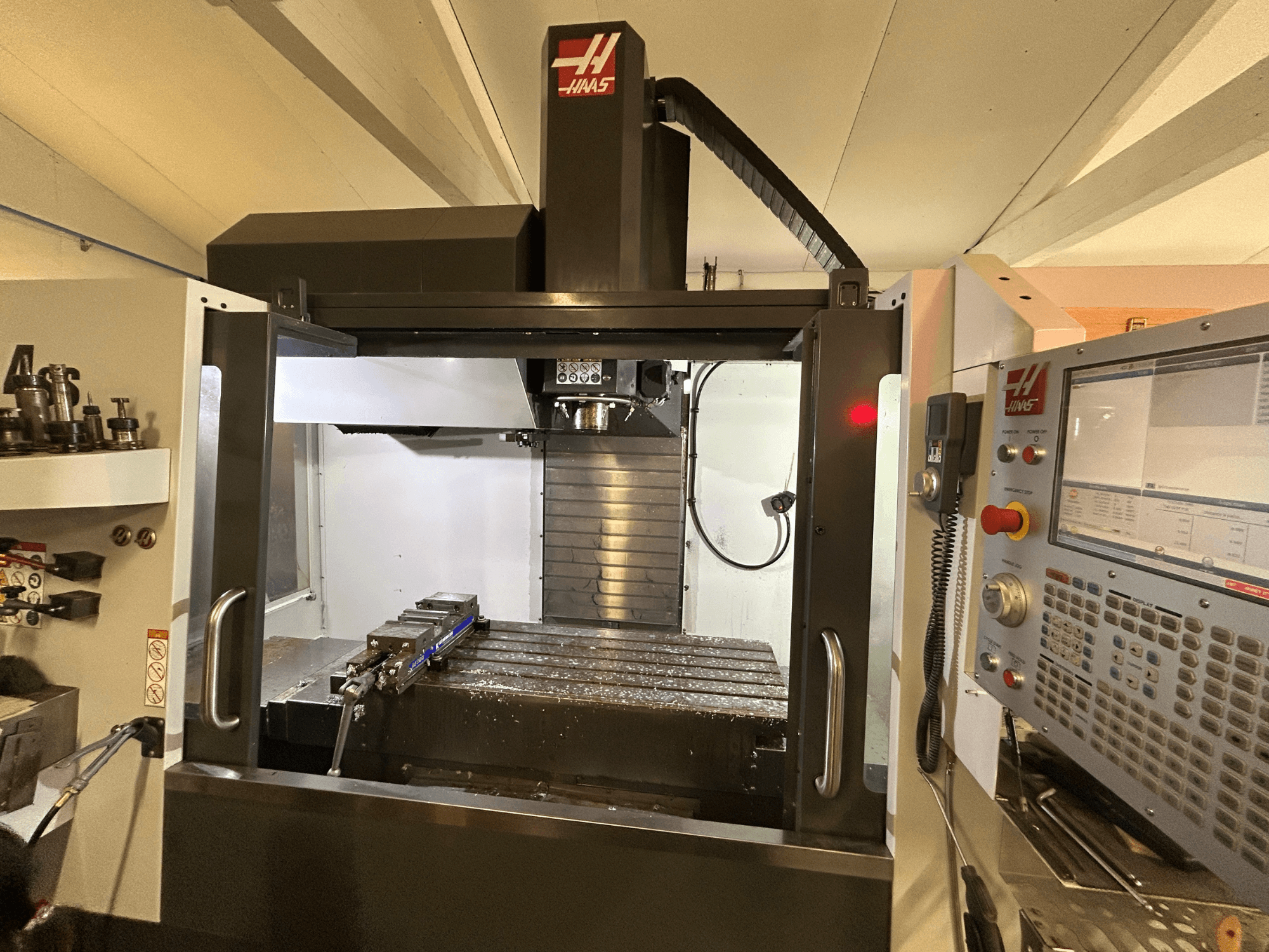 Pionowe centrum obróbcze HAAS VF-4SS, widok z przodu, panel sterowania, uchwyt narzędziowy i obszar roboczy z wiórami metalowymi.