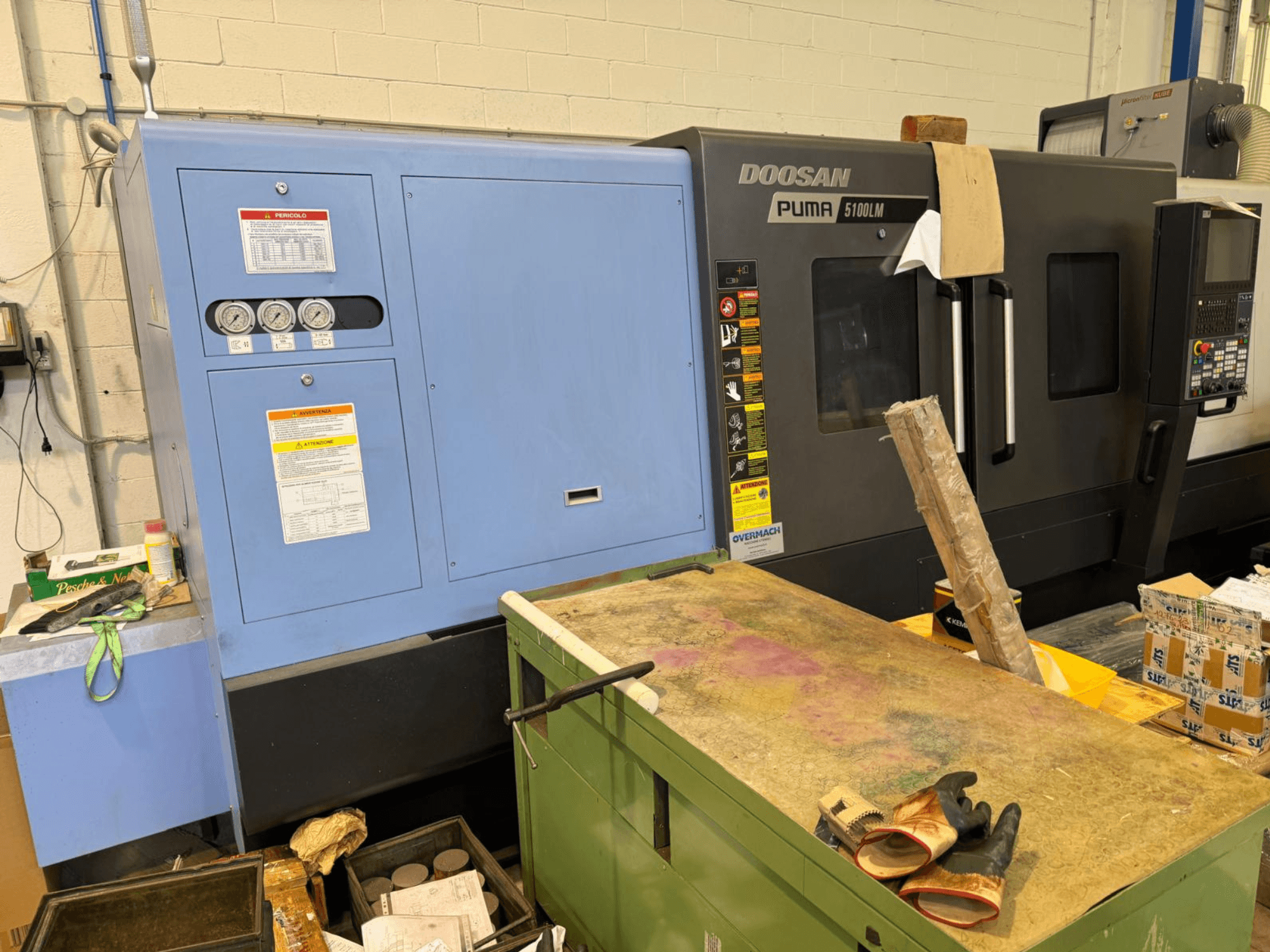 Maszyna CNC Doosan Puma 5100LM i panel sterowania, widok z boku. Wskaźniki i etykiety ostrzegawcze widoczne na niebieskiej jednostce sterującej.