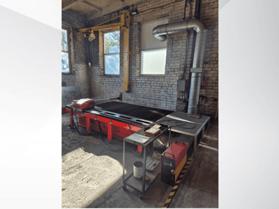 Czerwony stół CNC do cięcia plazmowego z panelem sterowania i metalowym kanałem wylotowym, widziany z boku w dobrze oświetlonym warsztacie.