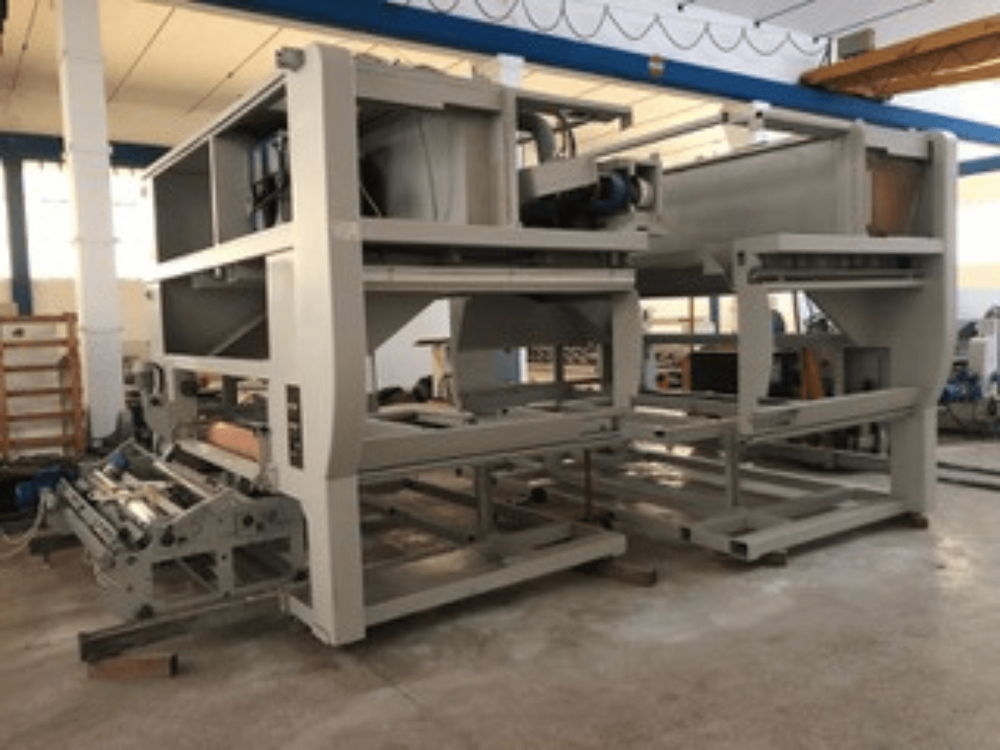 Maszyna przemysłowa z wieloma rolkami przenośnika i dużą konstrukcją; widok z boku, kolor szary, umieszczona w dobrze oświetlonej fabryce.