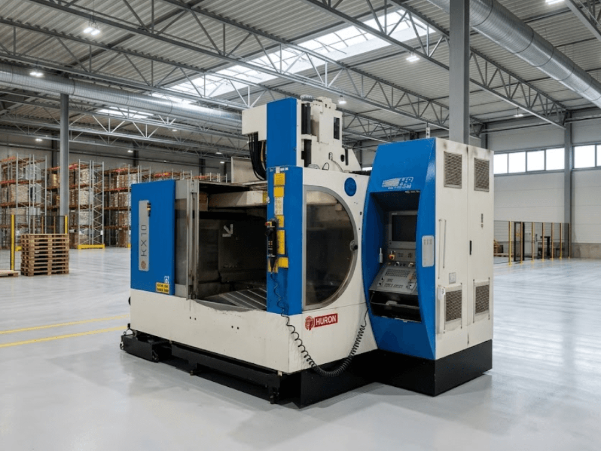 Pionowe centrum obróbcze Huron KX 10 w magazynie – widok z boku przedstawiający panel sterowania i otwartą przestrzeń roboczą.