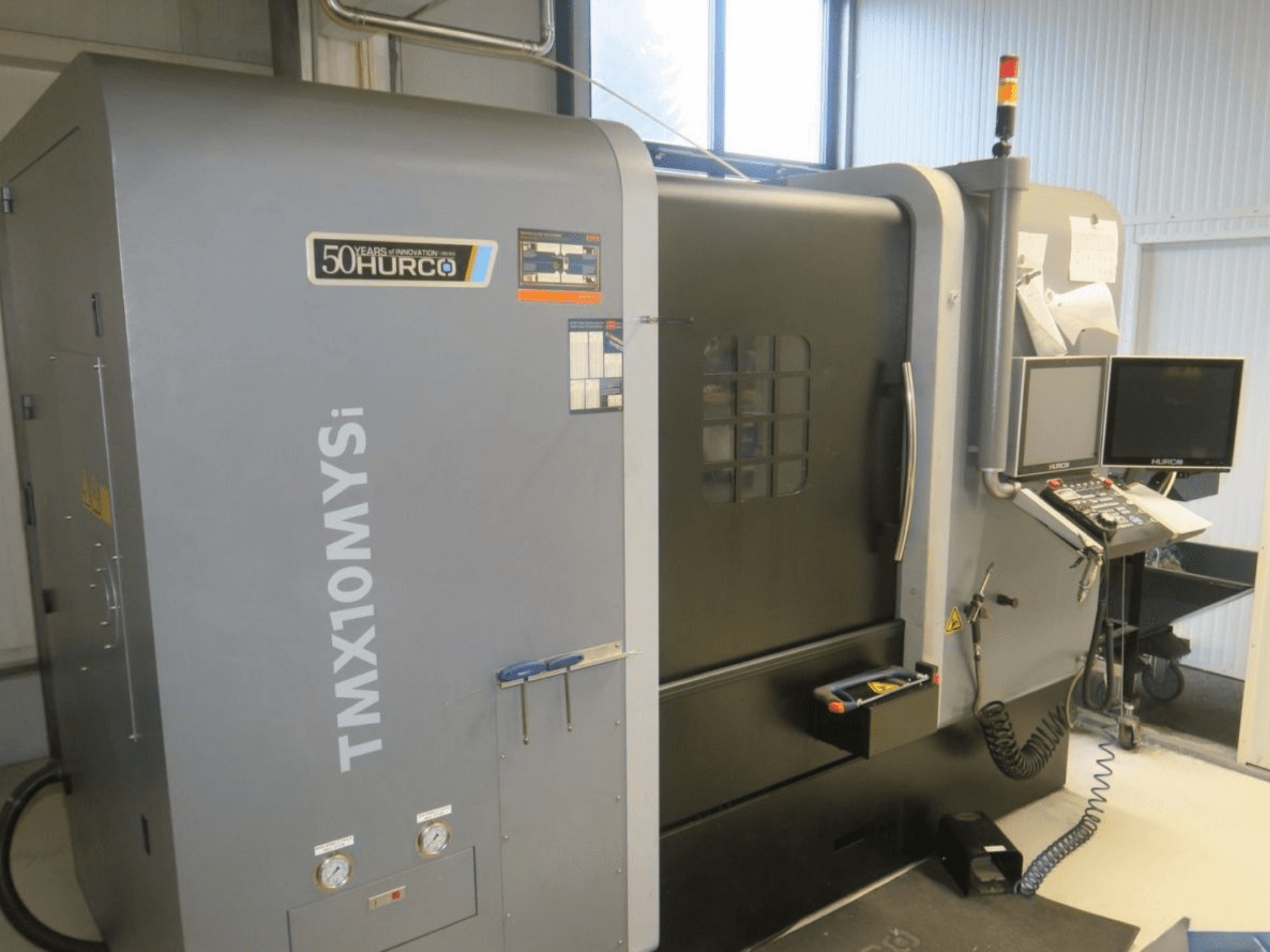Maszyna CNC Hurco TMX10MYSi w widoku z boku; posiada panel sterowania, światła awaryjne i wyświetlane wskaźniki.