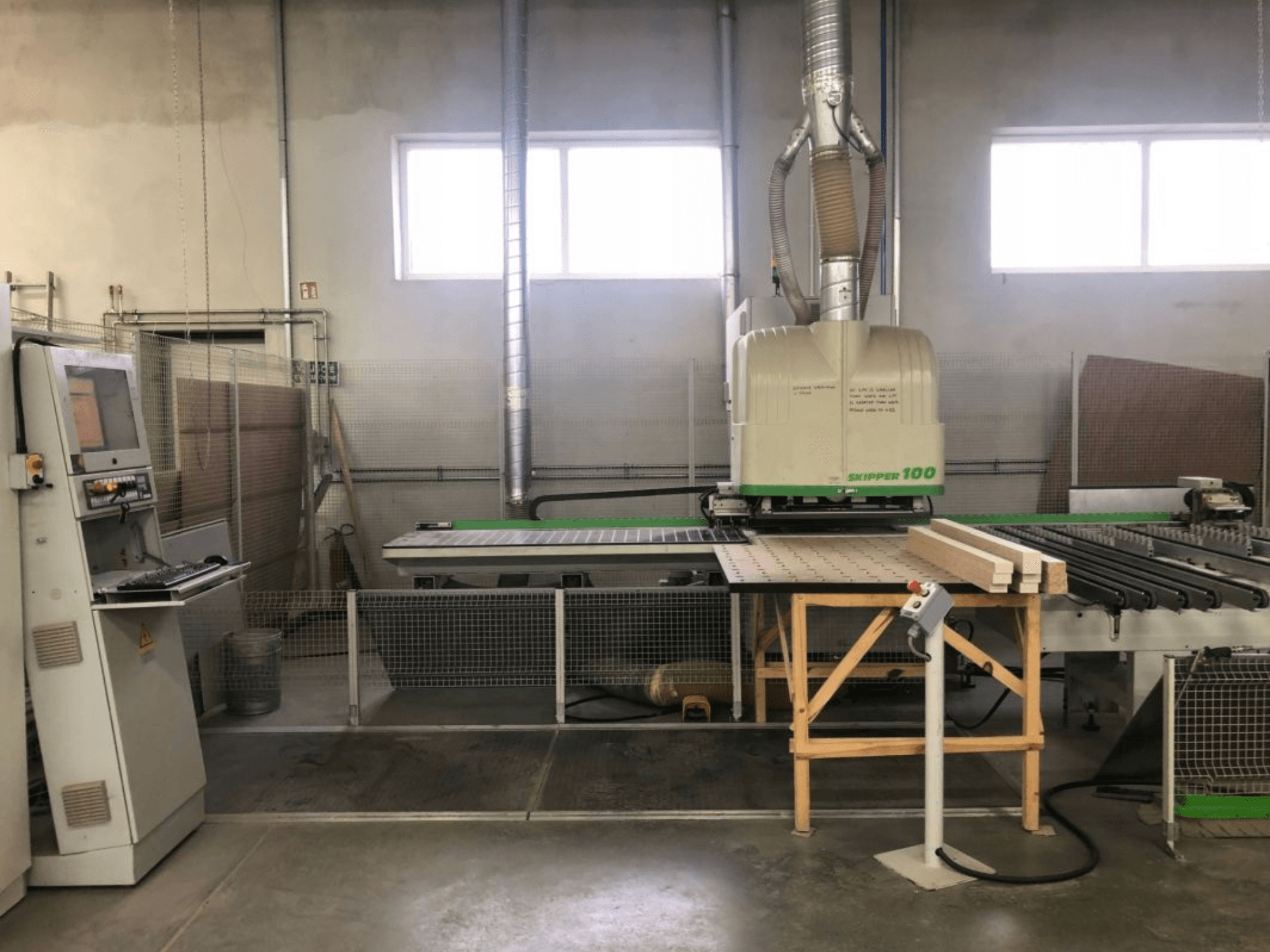Centrum obróbcze BIESSE SKIPPER 100 CNC w warsztacie; widok z przodu przedstawia maszynę z panelem sterowania i drewnem na stole.