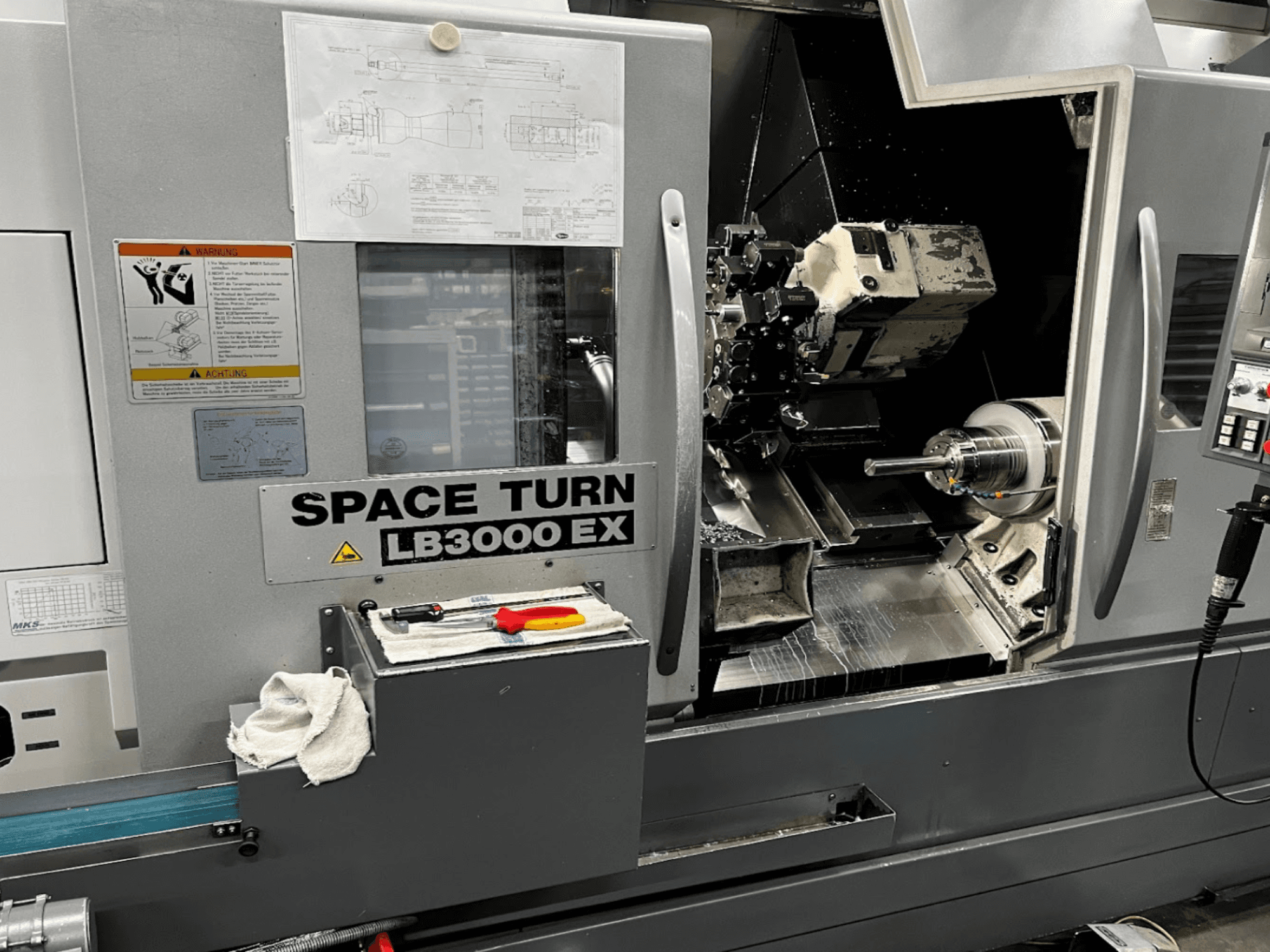 Tokarka pozioma Okuma LB3000EX MYW, widok z przodu z widocznym panelem sterowania, narzędziami i szczegółami przestrzeni roboczej.