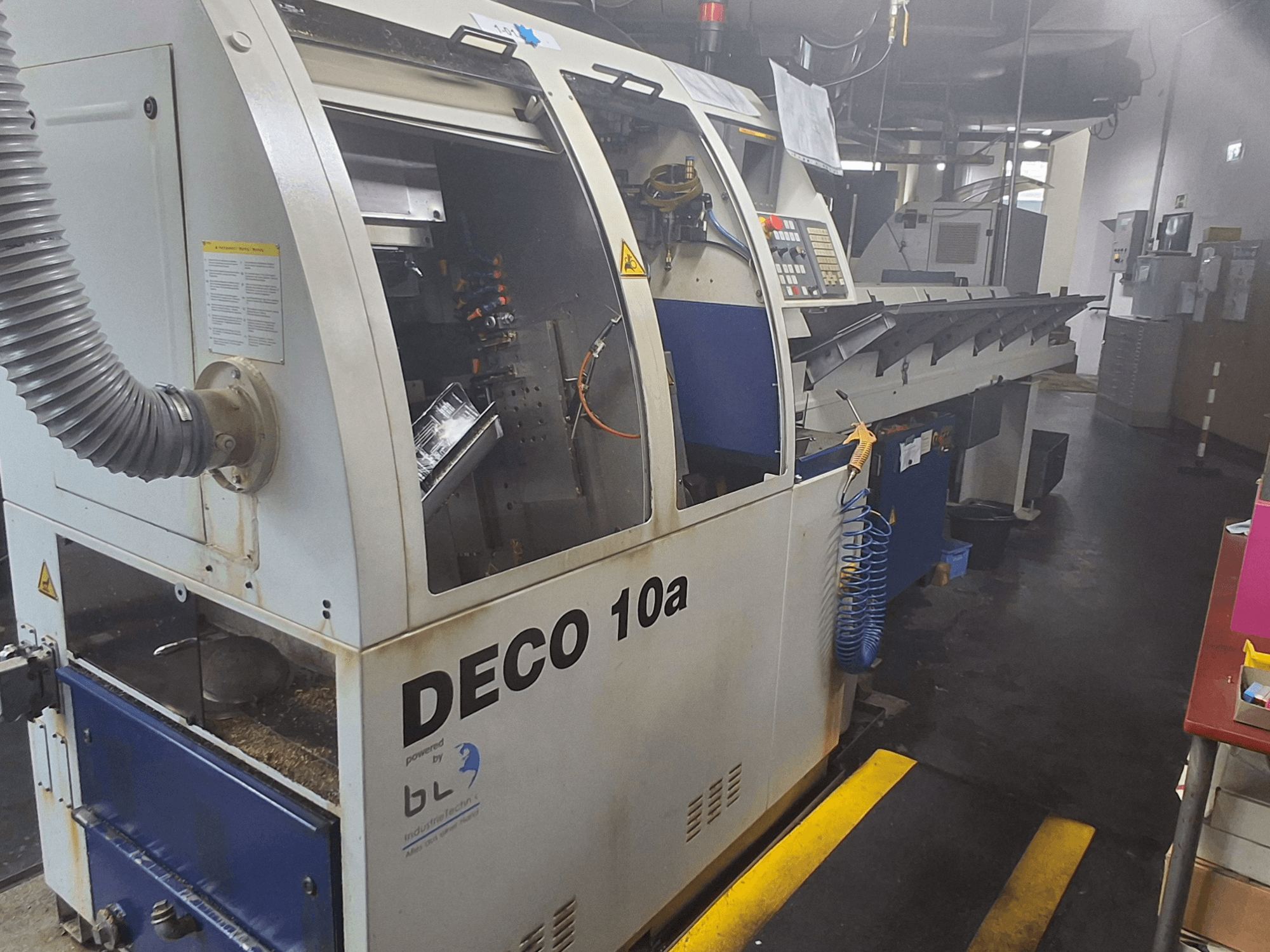 Tokarka szwajcarska TORNOS DECO 10a, widok z przodu; posiada panel sterowania, widoczne mechanizmy i rurę odpylającą.