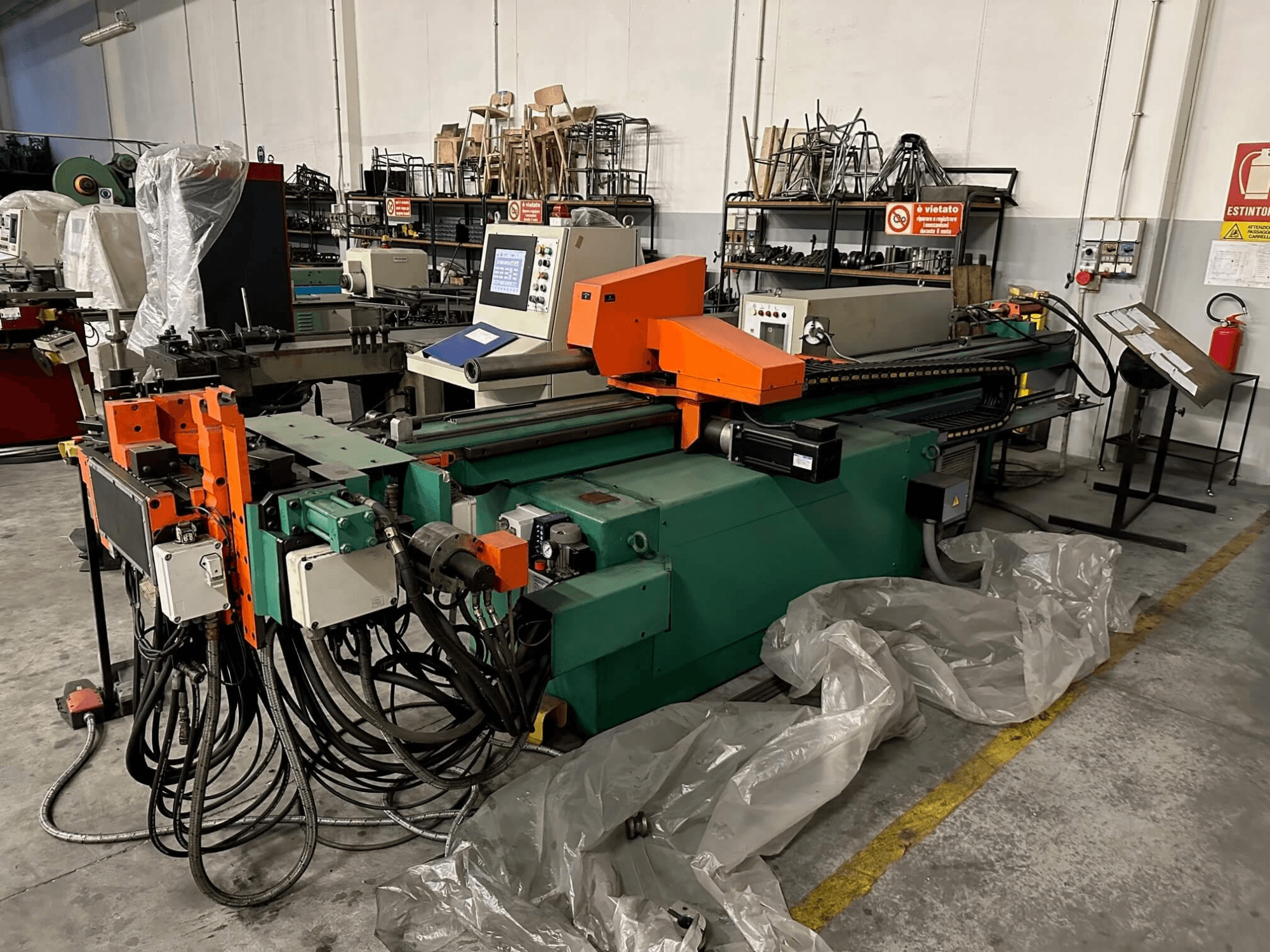 Maszyna przemysłowa z pomarańczowo-zielonym korpusem, panelem sterowania i licznymi kablami, widziana od przodu w warunkach warsztatowych.