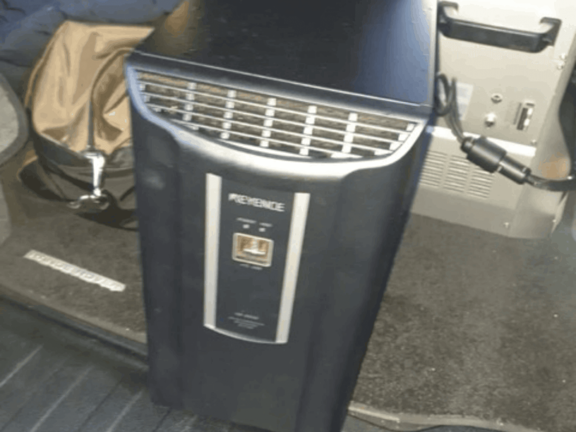 System automatyki KEYENCE IM-8030 w widoku z przodu, prezentujący panel sterowania i otwory wentylacyjne na tle wnętrza pojazdu.