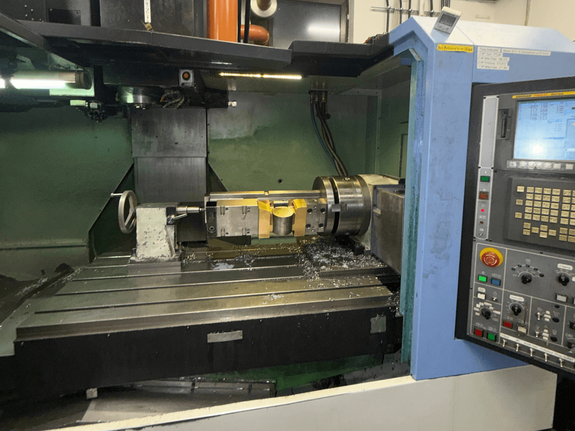 Pionowe centrum obróbcze DOOSAN DNM650, widok z przodu, przedstawiający narzędzie skrawające i panel sterowania, z wiórami metalowymi widocznymi na stole.