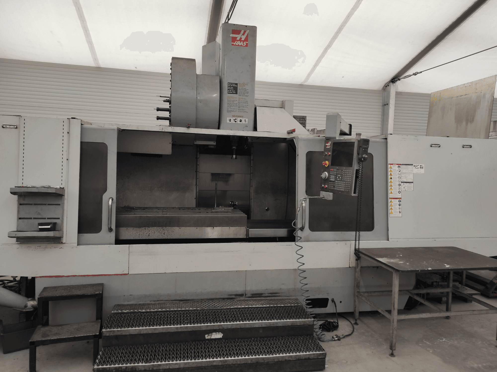 Pionowe centrum obróbcze HAAS VF-10/50HE, widok z przodu przedstawiający panel sterowania, łoże maszyny i dostępny stopień do obsługi.