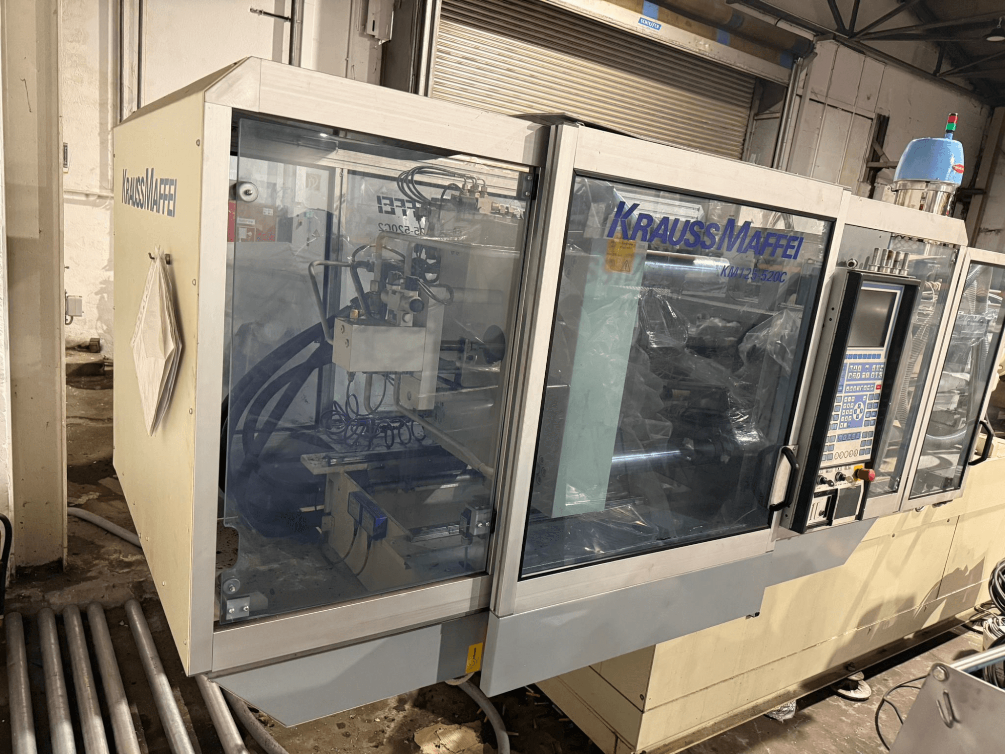 Hydrauliczna wtryskarka Krauss Maffei KM125-520C2, widok z przodu z panelem sterowania i przezroczystą obudową.